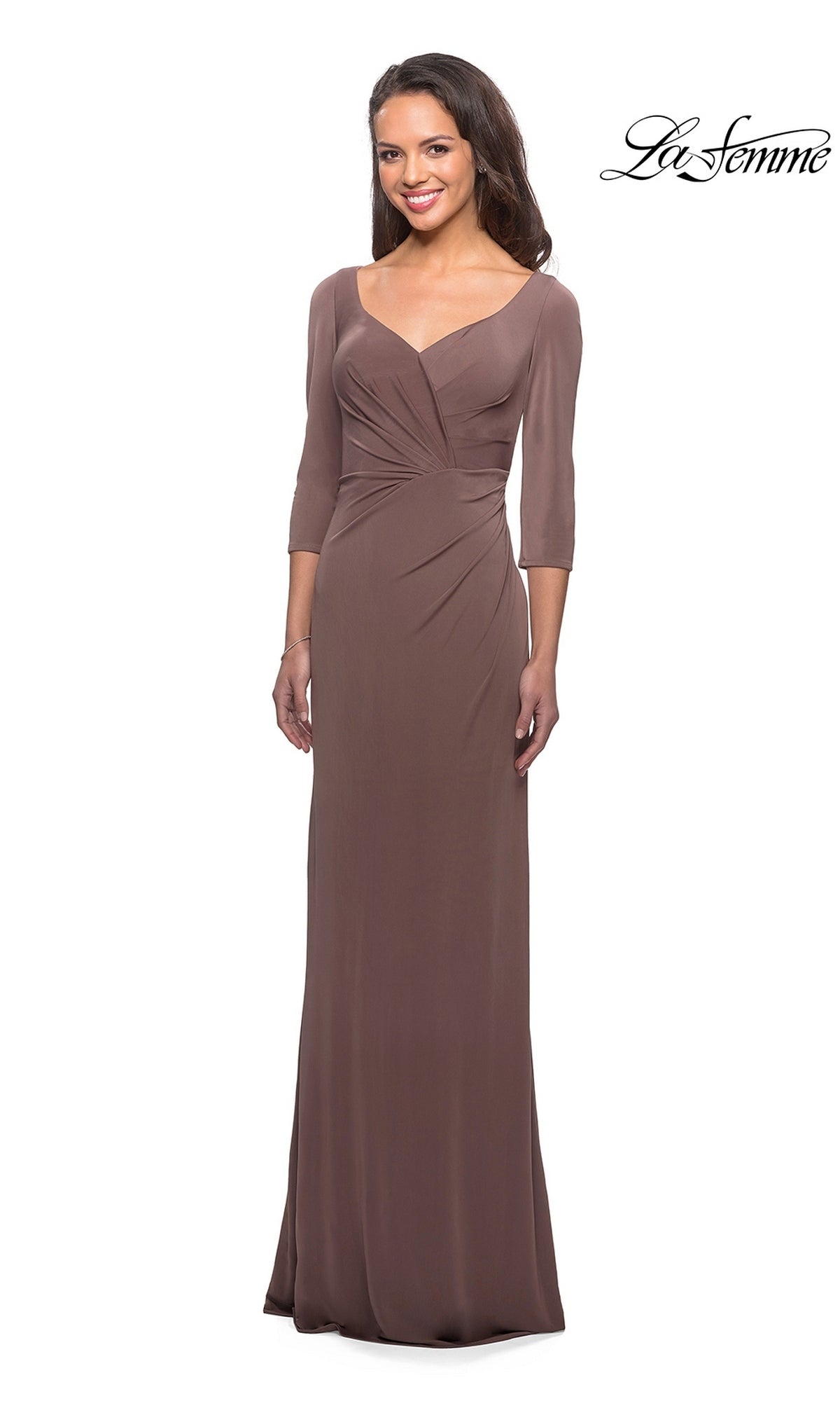 A woman wearing the La Femme 26955 long formal dress in cocoa, featuring three-quarter length sleeves, a V-neckline, and a fitted sheath skirt, poses and smiles against a plain white background.