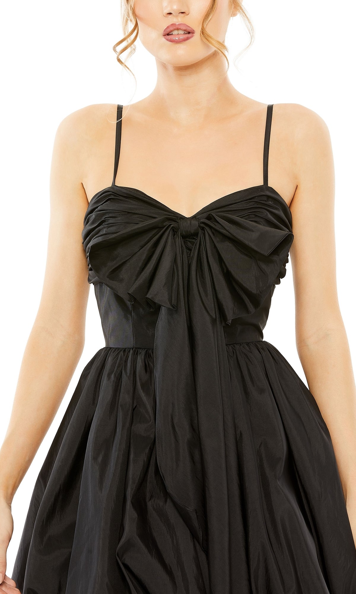 A woman wears the Short Party Dress 27040 by Mac Duggal, featuring black fabric, spaghetti straps, a large front bow detail, and a full skirt.