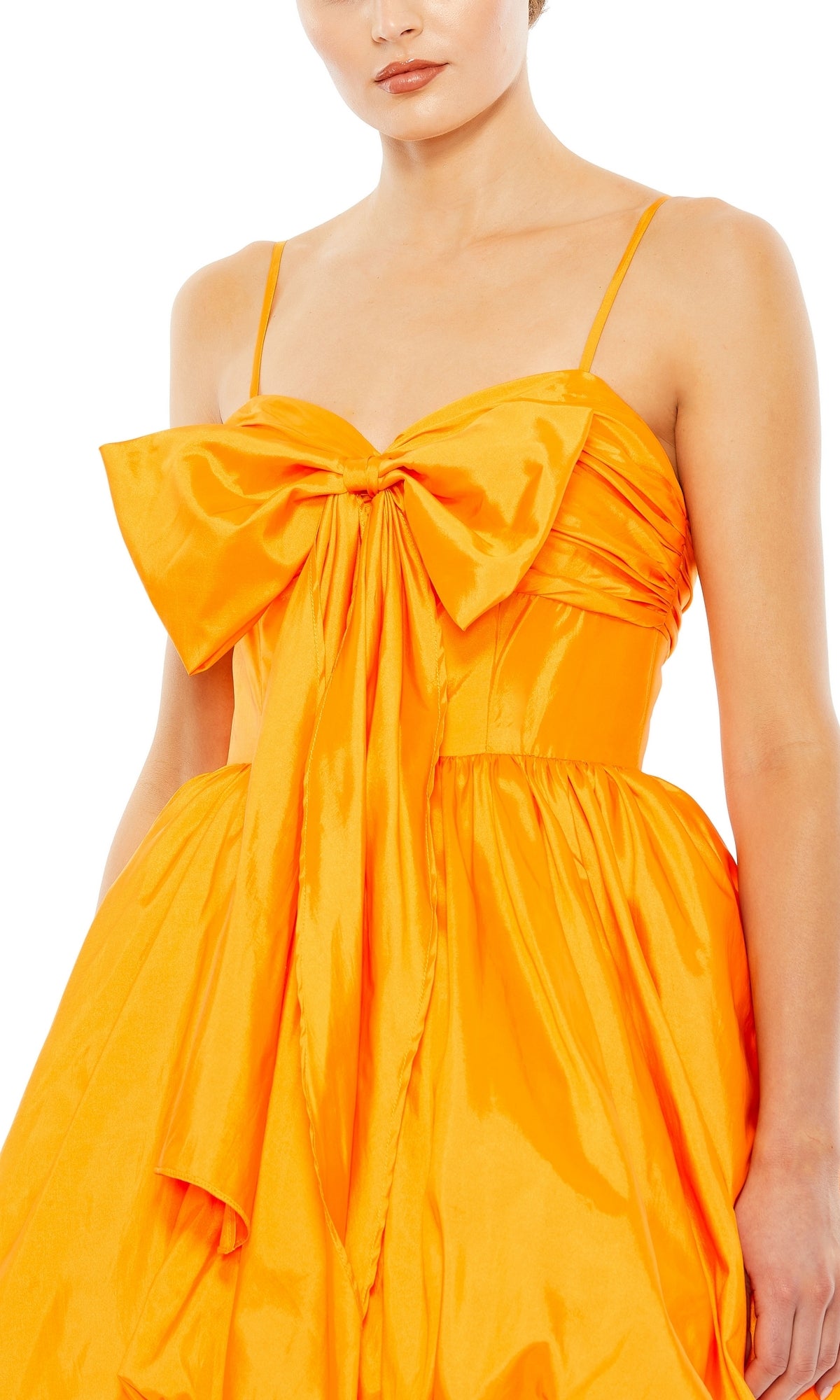 Model in the Short Party Dress 27040 by Mac Duggal, a shiny orange gown with thin straps and a large bow on the chest, shown from shoulders to mid-thigh against a white background.