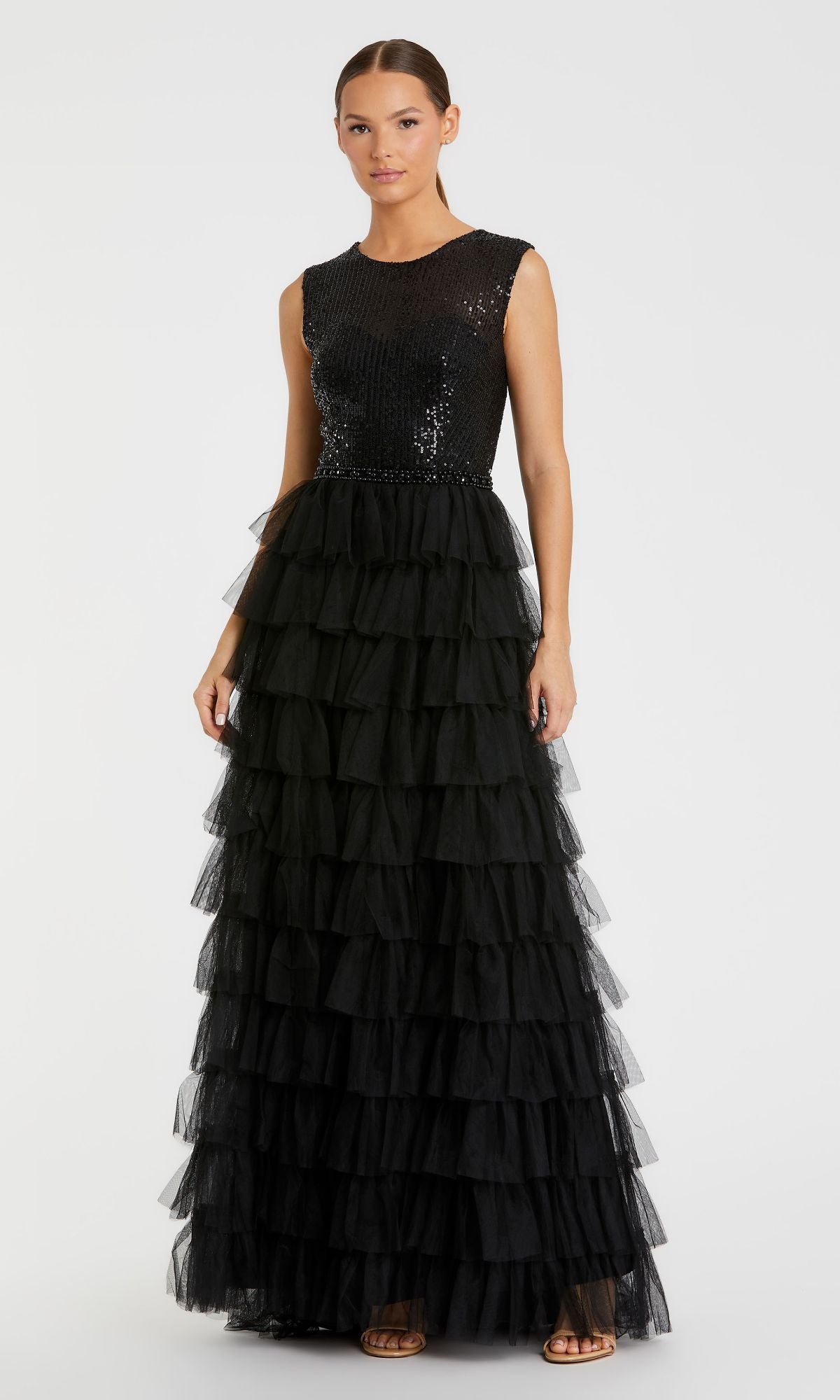 A woman wears the Mac Duggal 27055, a long black ruffled formal dress with a sequined bodice and tiered tulle skirt, paired with open-toe heels.