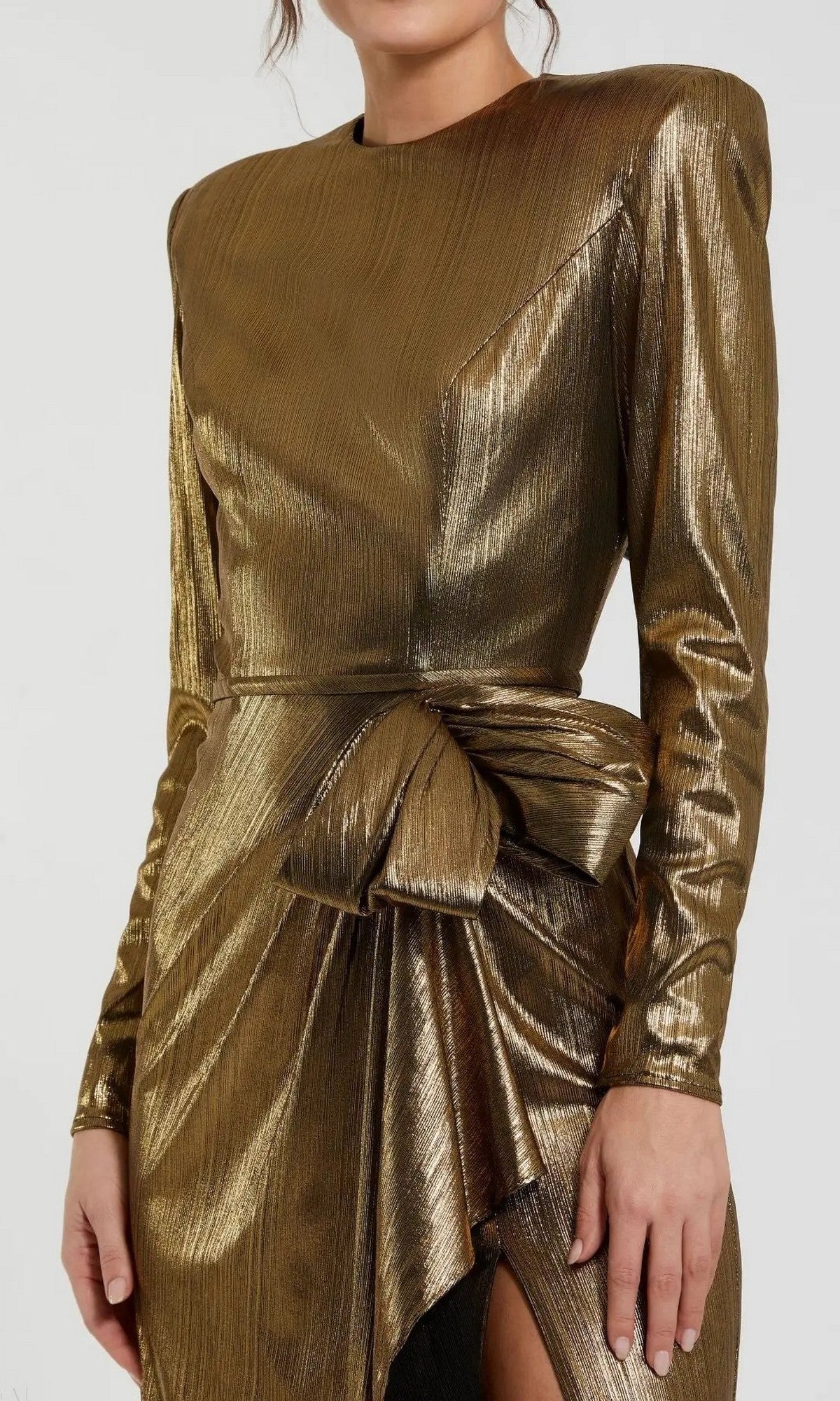 A person wearing the Mac Duggal 27206 long formal dress in metallic gold, featuring long sleeves, structured shoulders, and a prominent bow accent at the waist.