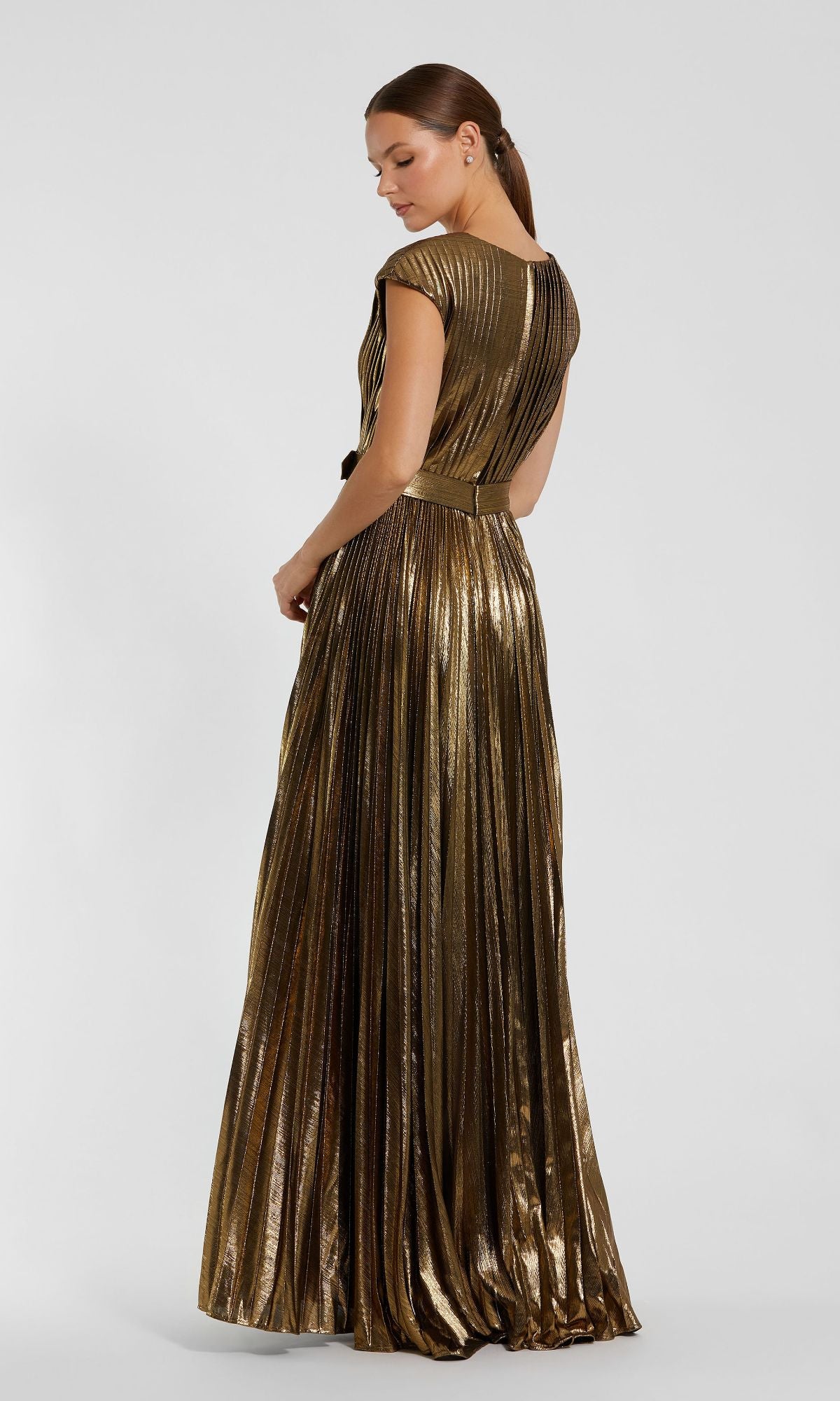 A woman in profile models the Pleated Long Bronze Evening Gown, Mac Duggal 27215โan elegant floor-length dress with cap sleeves, a defined waistband, and metallic pleats.