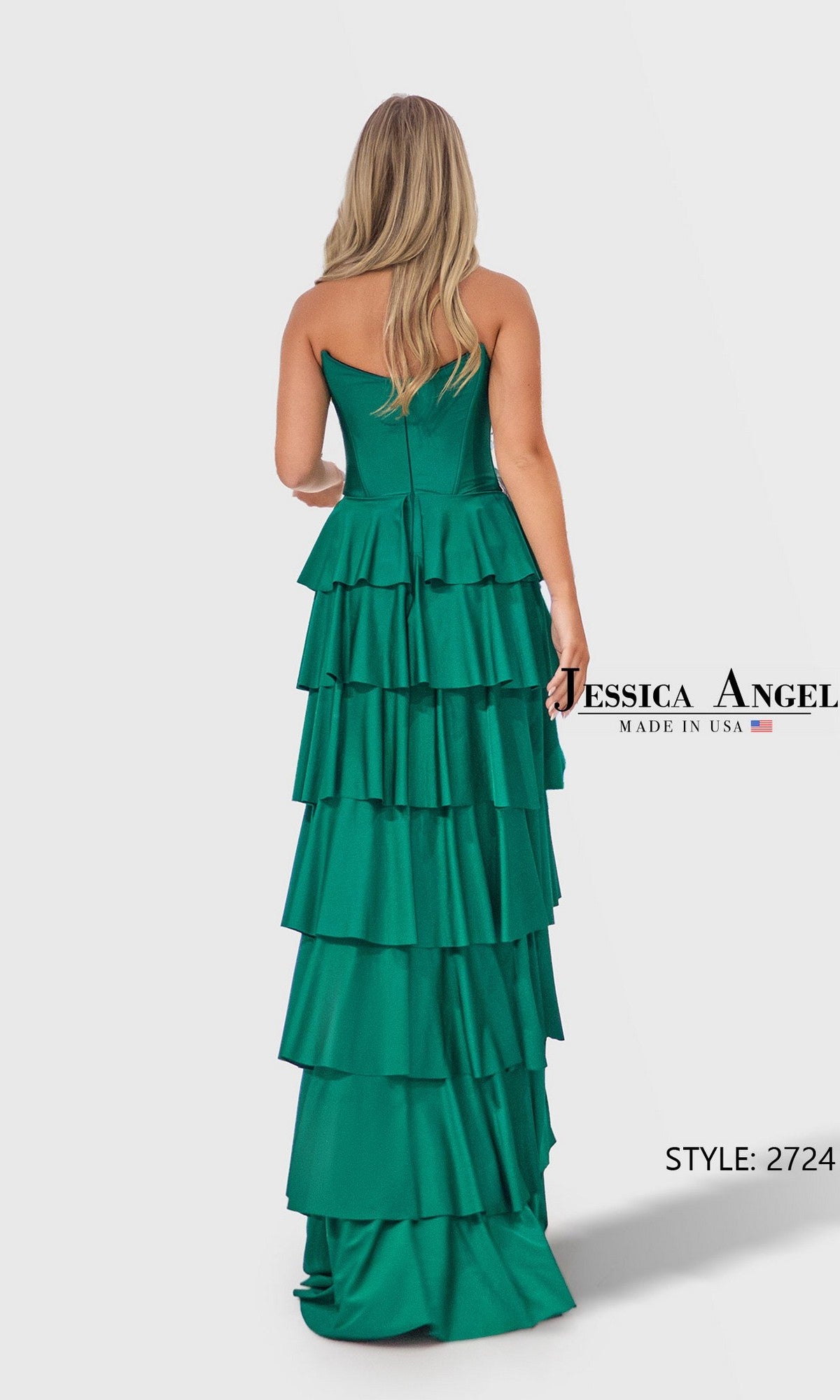A woman in an emerald green strapless jersey prom dress with a corset bodice and dramatic ruffle tiered skirt stands facing away. The floor-length gown is labeled