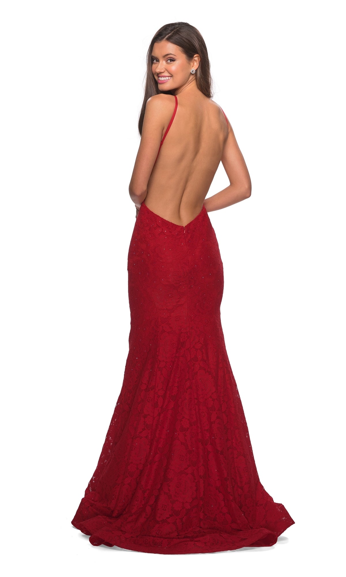 A woman stands smiling over her shoulder in the La Femme Floral Lace Mermaid Prom Dress 27289, a backless, floor-length gown with an open low V-back, against a plain white background.
