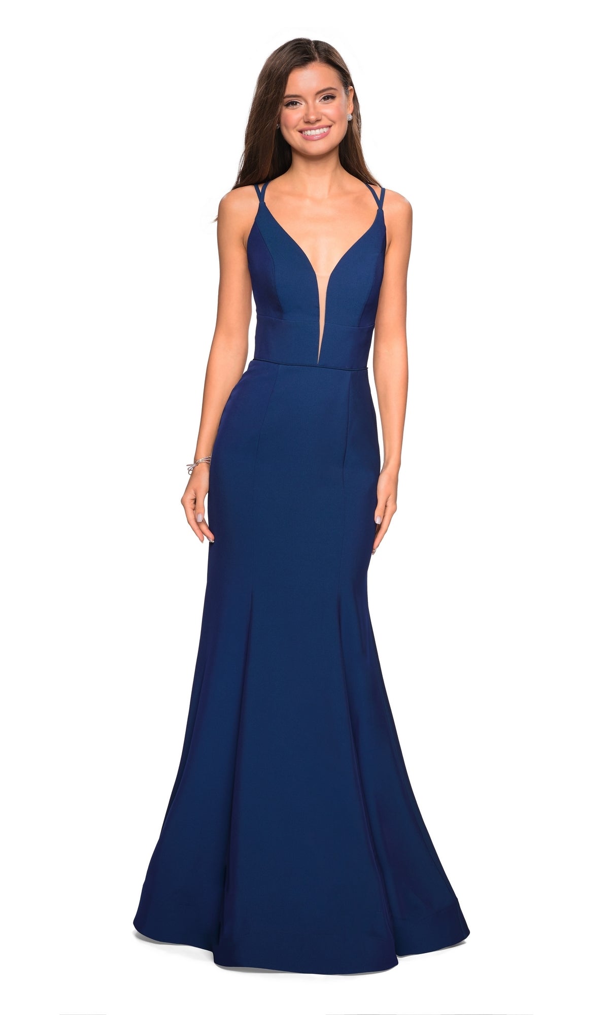 A woman stands and smiles against a white background in the La Femme Open-Back V-Neck Jersey Prom Dress 27446, a sleeveless, floor-length deep blue mermaid gown with a deep V neckline and open back.