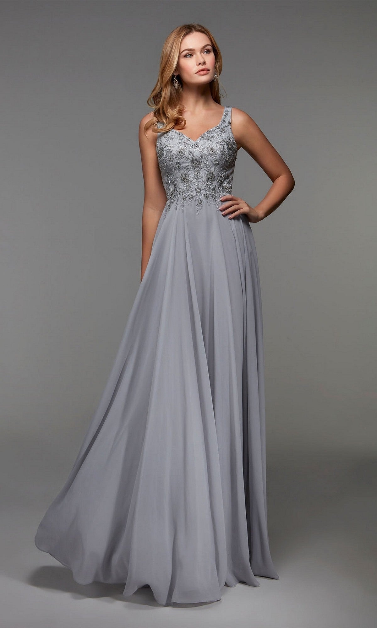 A woman poses against a plain gray background in the Alyce 27473 long formal dress. The sterling chiffon A-line gown, featuring an embellished bodice and flowing skirt, adds elegance to her graceful look.