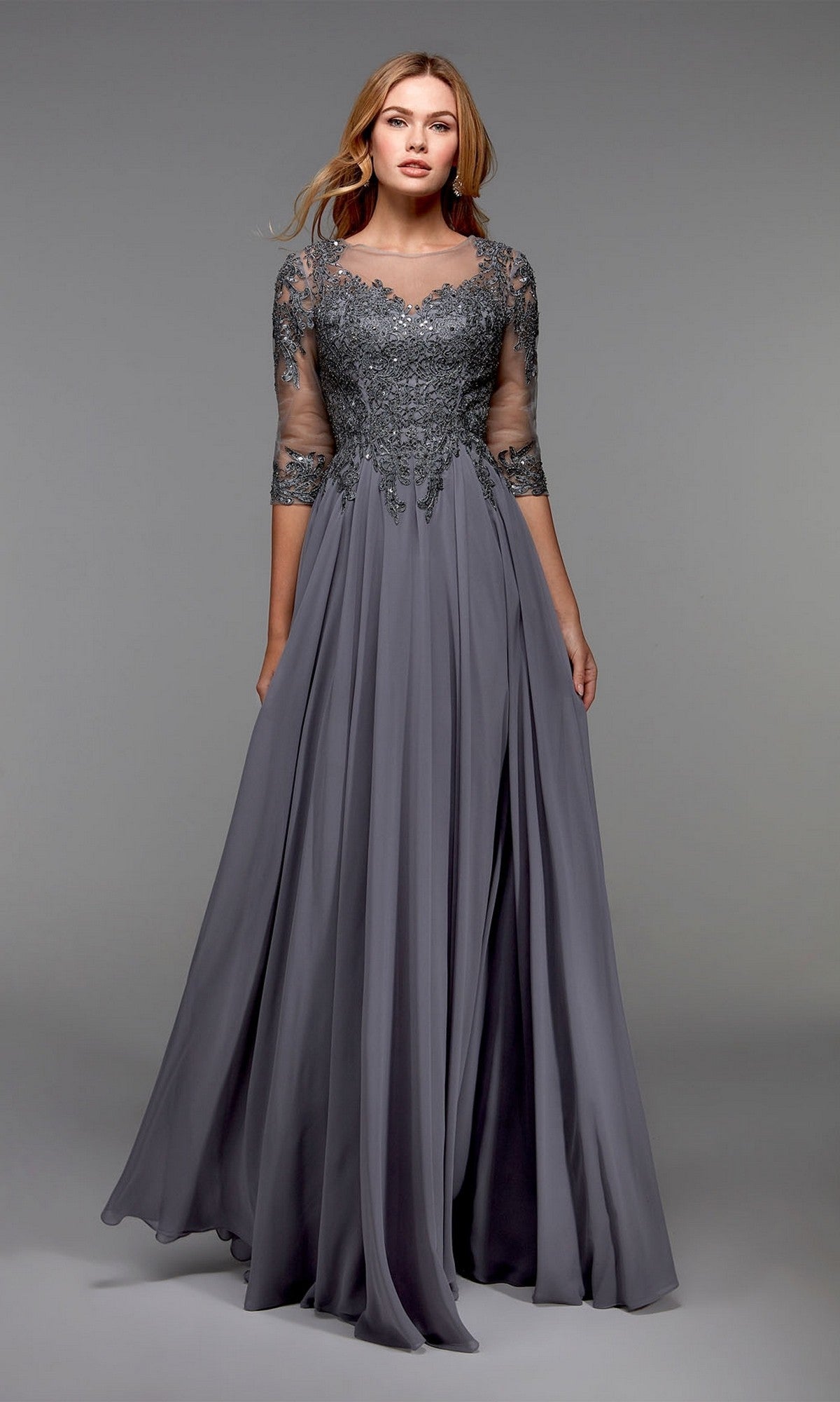 A woman wears the Alyce 27474 long formal dress—an elegant grey mother-of-the-bride gown featuring an embellished bodice and lace sleeves—standing against a plain grey background.