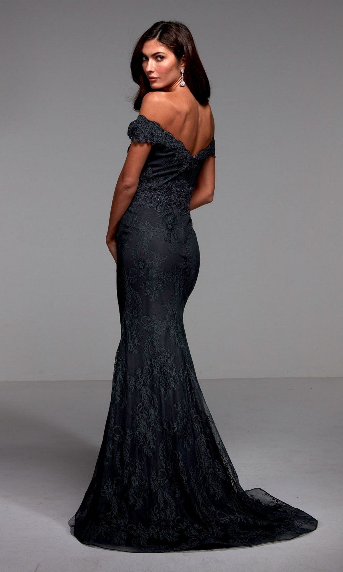 A woman wears the Long Formal Dress: Alyce 27484, standing in a plain studio and looking over her shoulder.