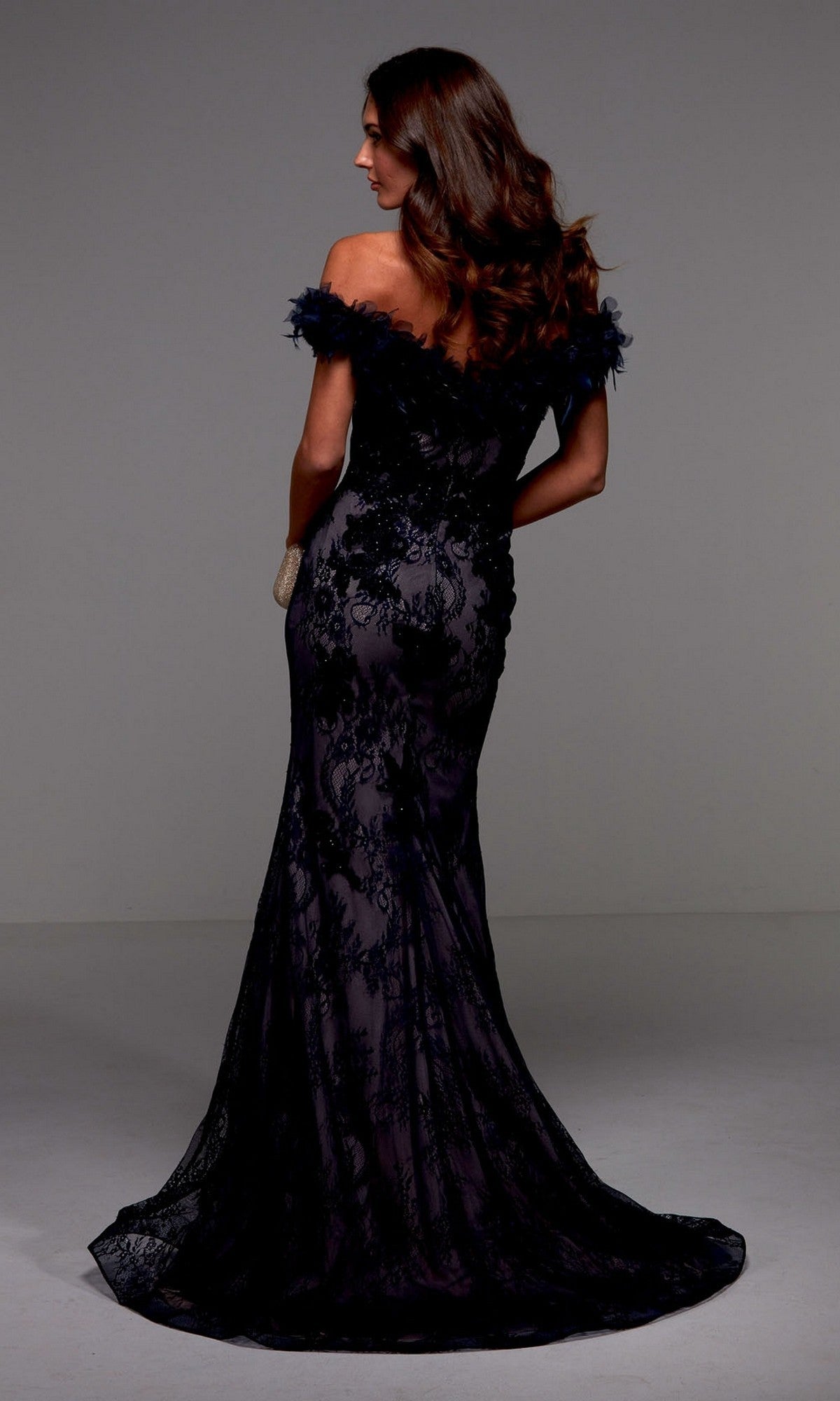 A woman faces away from the camera, wearing the Alyce 27490 long formal dress with lace detailing, an off-the-shoulder neckline, a fitted mermaid silhouette, and a dramatic floor-length train.
