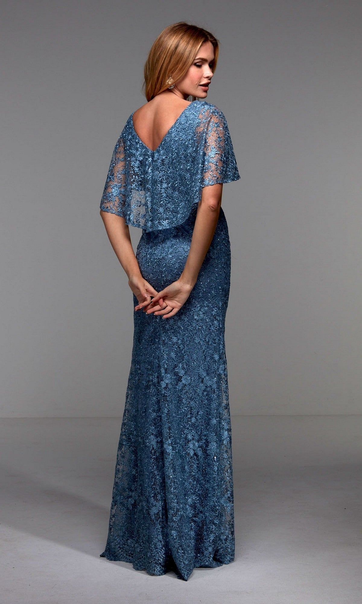 A woman stands with her back to the camera, wearing the Alyce 27506— a floor-length dark blue lace formal dress with short sleeves and a V-back, perfect as a mother of the bride dress.