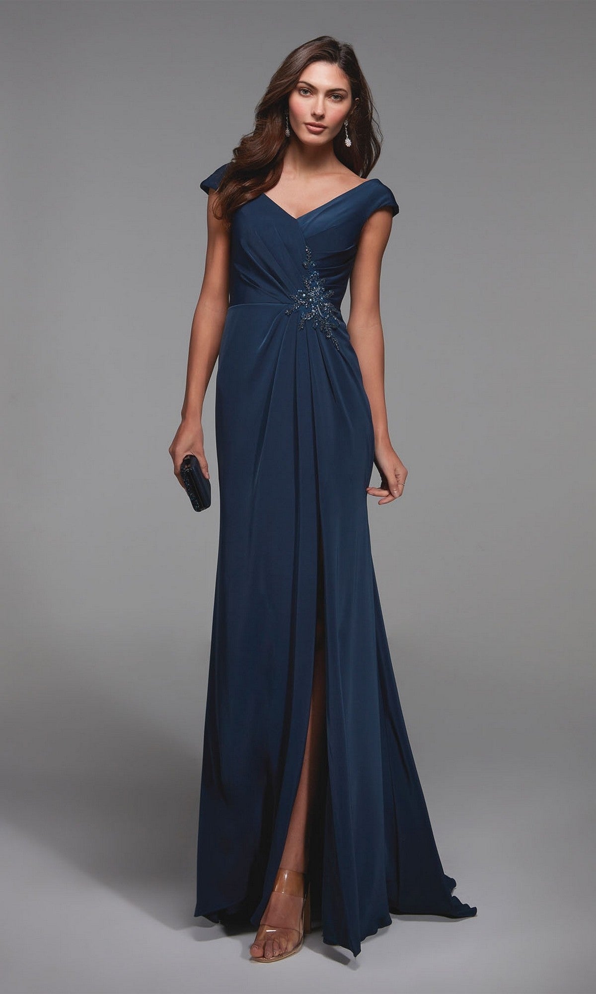 Woman in the Alyce 27508 long formal dress in Blue Opal with cap sleeves, v-neckline, and beaded waist detail, paired with a black clutch and strappy heels—an elegant choice for a mother-of-the-bride.