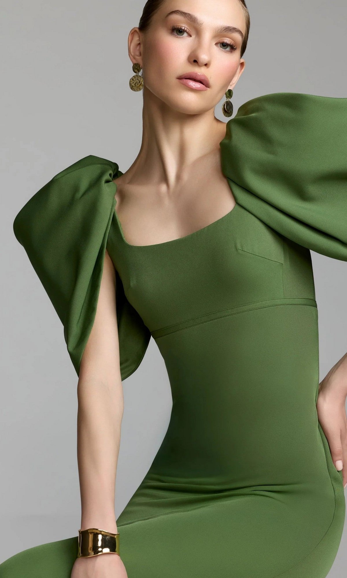 A woman in the Mac Duggal 27534 Puff-Sleeve Long Formal Dress, styled with gold earrings and a bracelet, poses against a plain grey background.