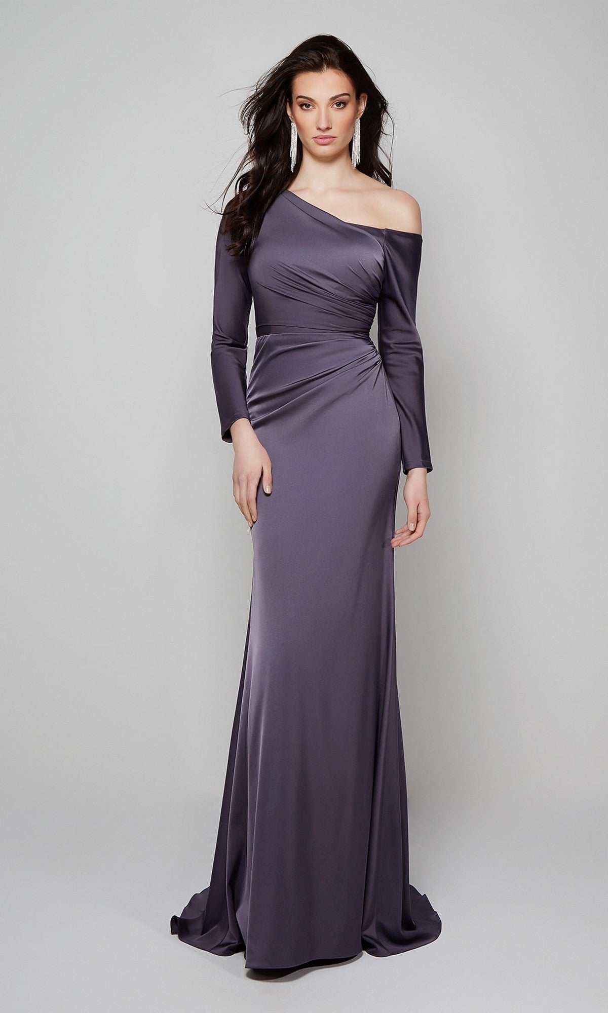 A woman models the Long Formal Dress Alyce 27557 in graphite, featuring a fitted silhouette, one long sleeve, and an off-the-shoulder neckline against a plain light background.