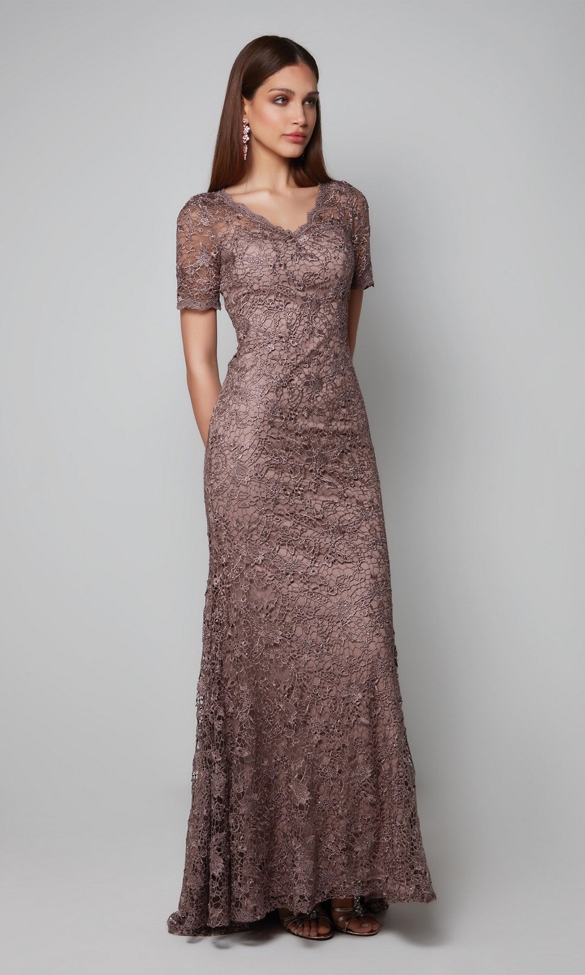 A woman stands against a plain background wearing the Long Formal Dress: Alyce 27561 in mauve with short sleeves, styled with earrings and sandals.