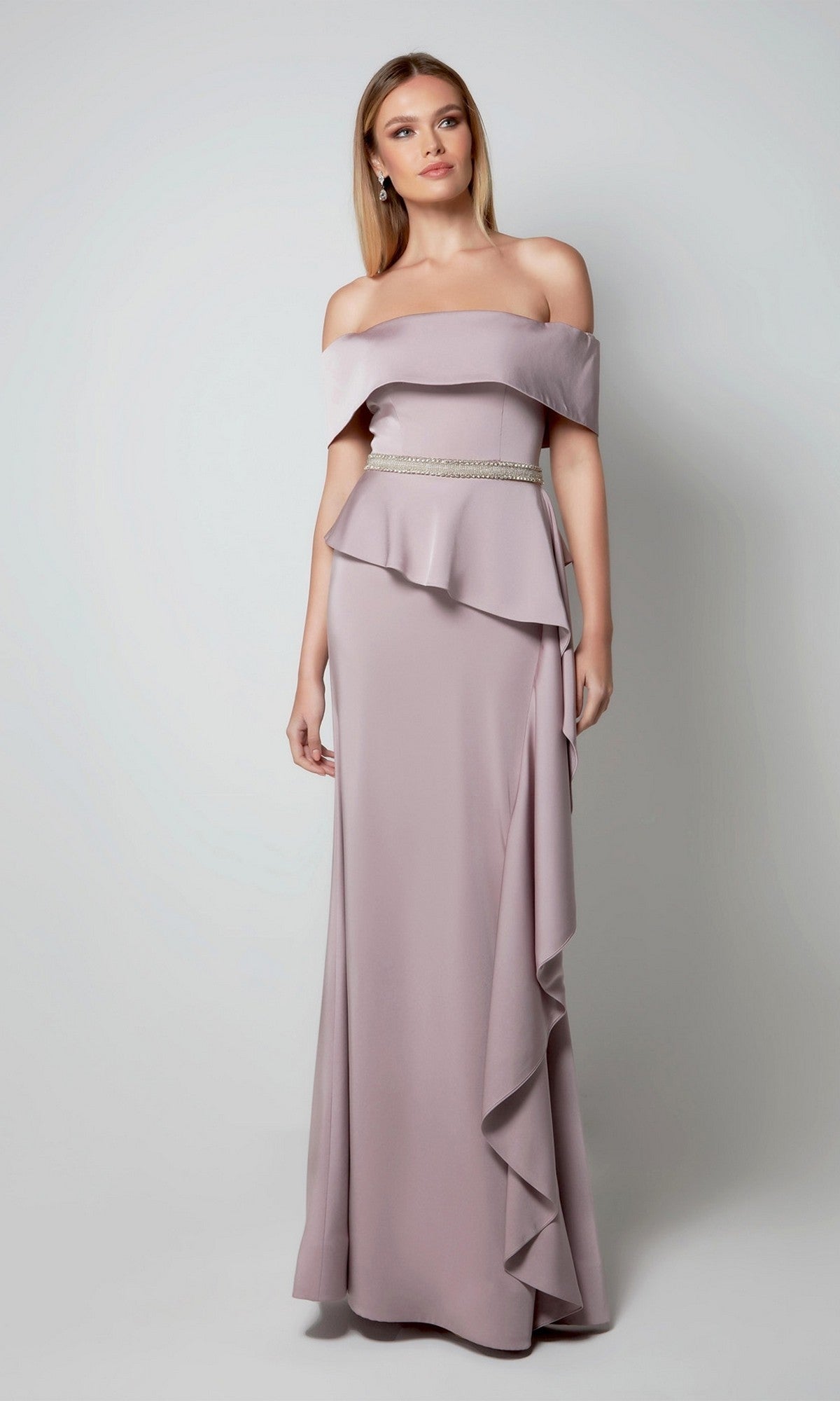 A woman in the Alyce 27563 long formal dress in soft heather, featuring off-the-shoulder styling, a ruffled peplum, and beaded waist detail, stands against a plain light background—ideal for a stylish mother-of-the-bride look.