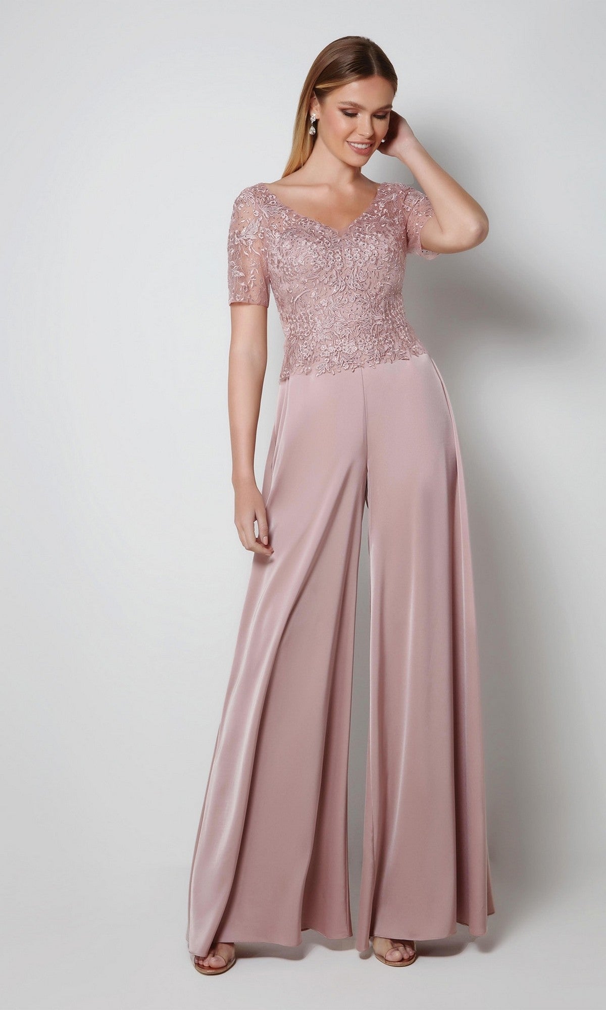 Woman smiling with one hand in her hair, wearing the Alyce 27564 long formal dress in Cashmere Rose—an elegant choice for the mother of the bride, featuring an embroidered bodice, against a plain light background.