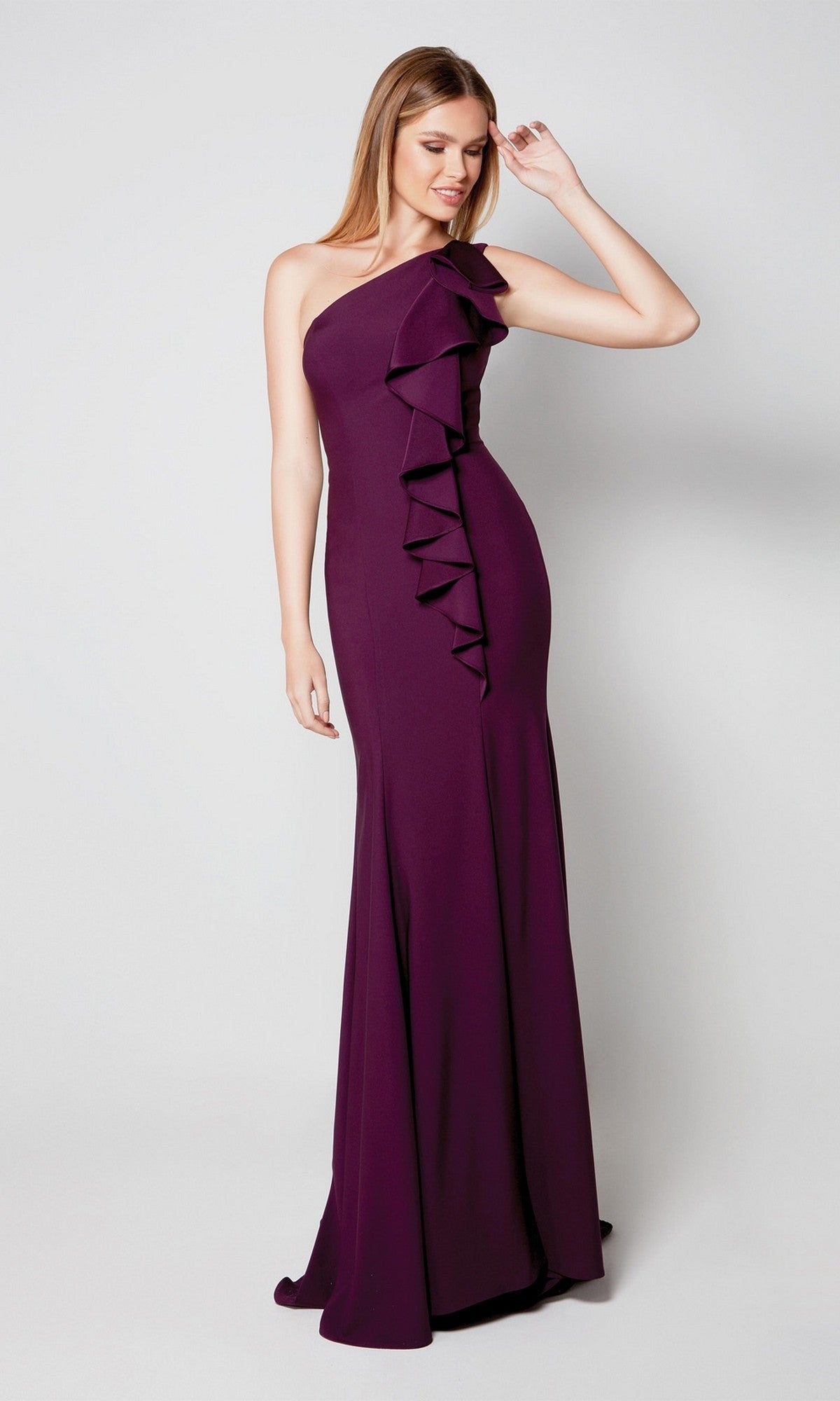 A woman models the Long Formal Dress: Alyce 27575, an elegant amethyst one-shoulder gown with ruffle detailing, standing against a plain light background.