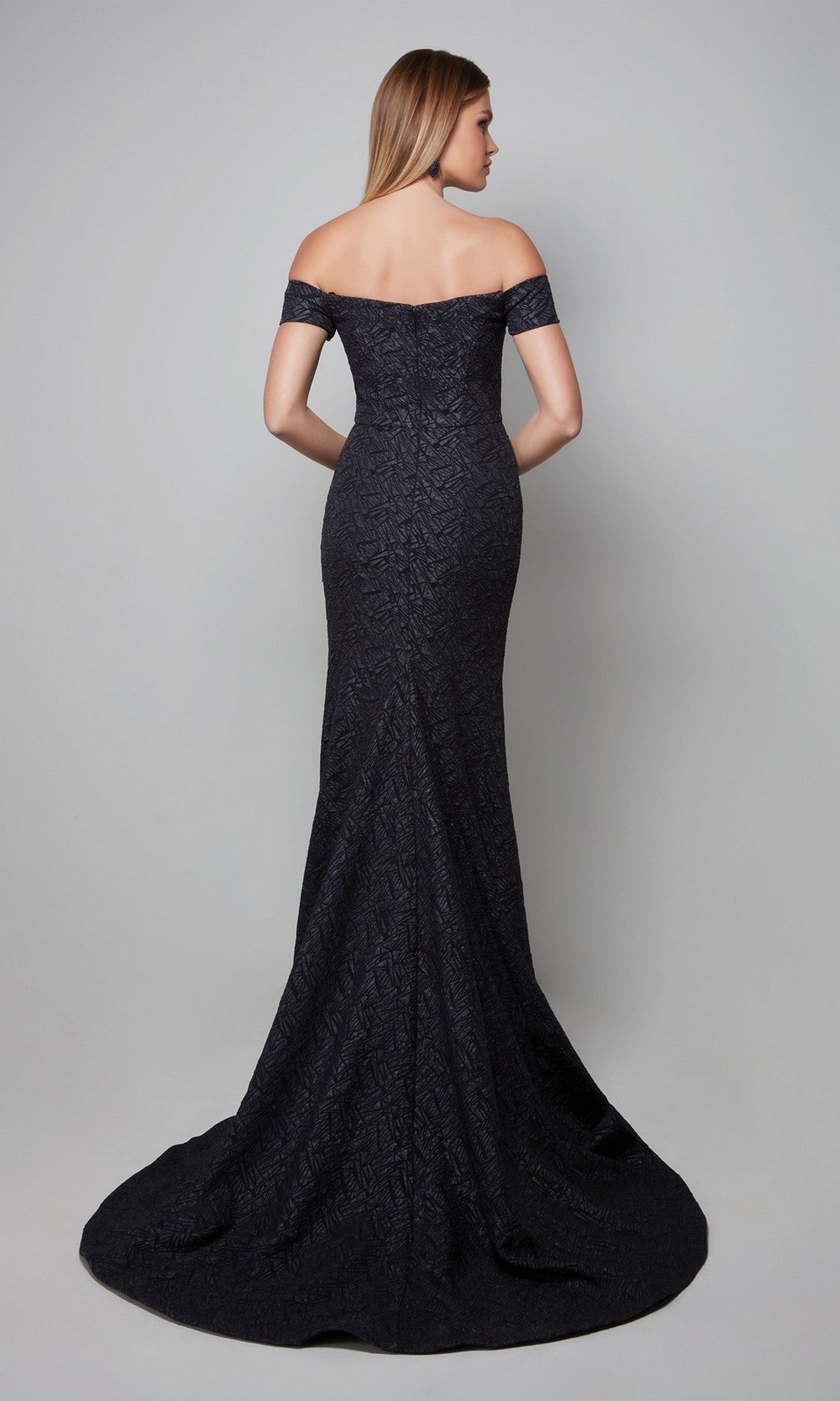 A woman stands with her back to the camera against a plain grey background, wearing the Alyce 27578, a fitted, off-the-shoulder black floor-length formal dress.