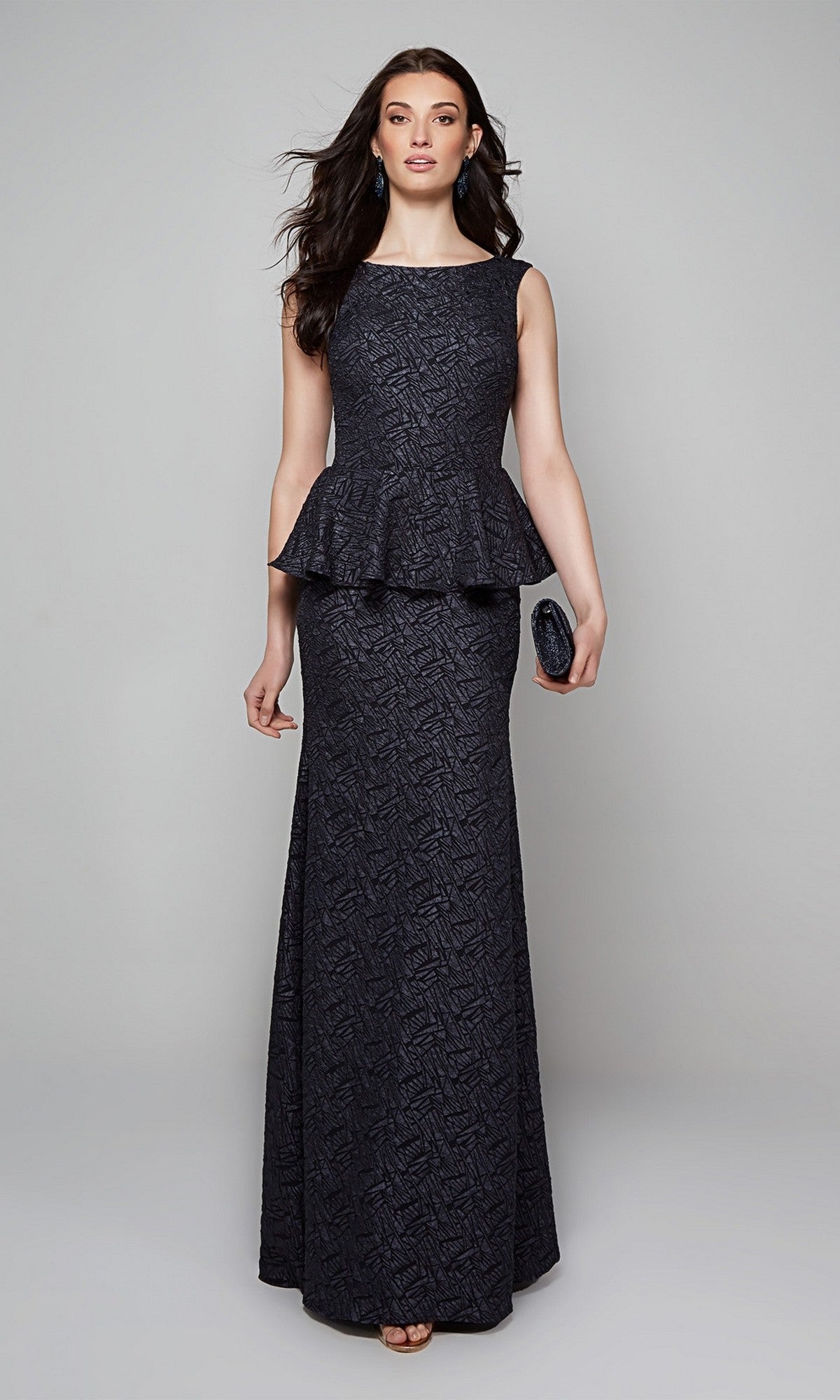 A woman in the Alyce 27579 long formal dress, a sleeveless dark jacquard peplum gown, holds a small clutch and stands against a plain light gray background.