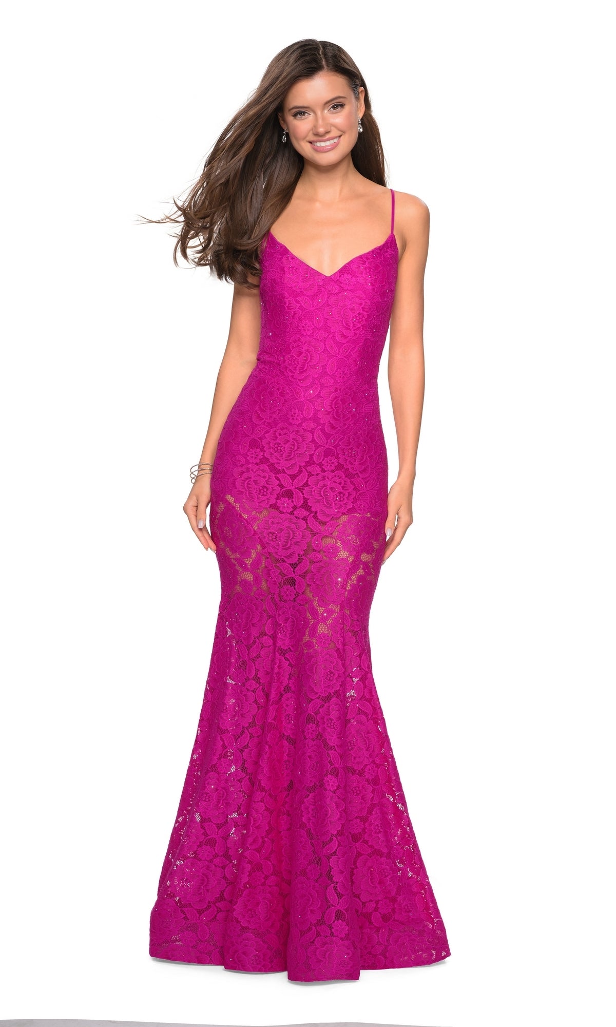 Woman wearing a fitted, floor-length hot pink Sheer Lace Mermaid Prom Dress (La Femme 27584) with spaghetti straps and an open back, smiling against a plain white background.