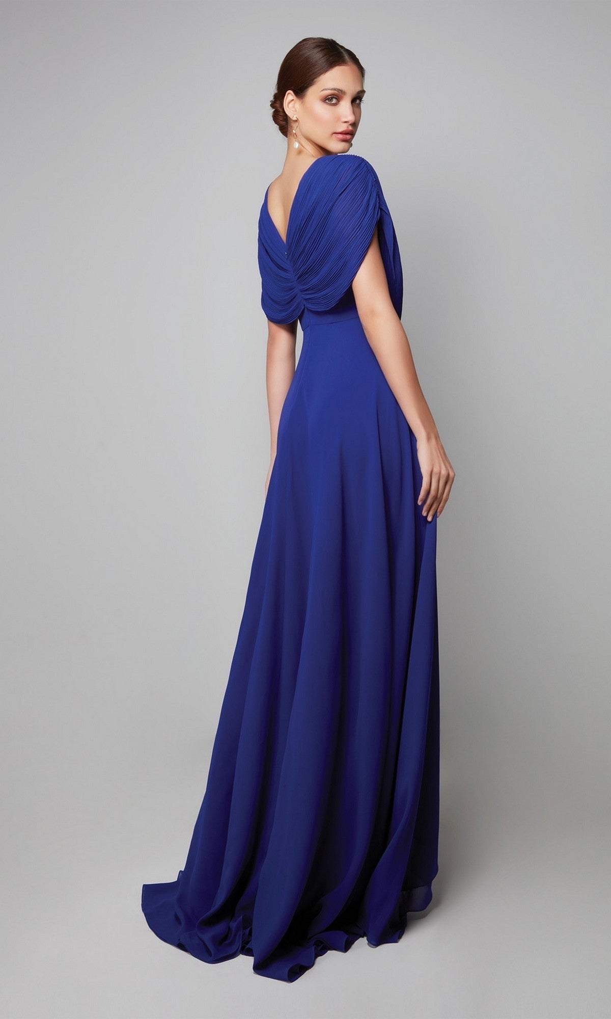 Woman wearing the Alyce 27592 long formal dress in royal blue, featuring chiffon fabric, elegant cape sleeves, and draped back detailing, standing against a plain gray background.