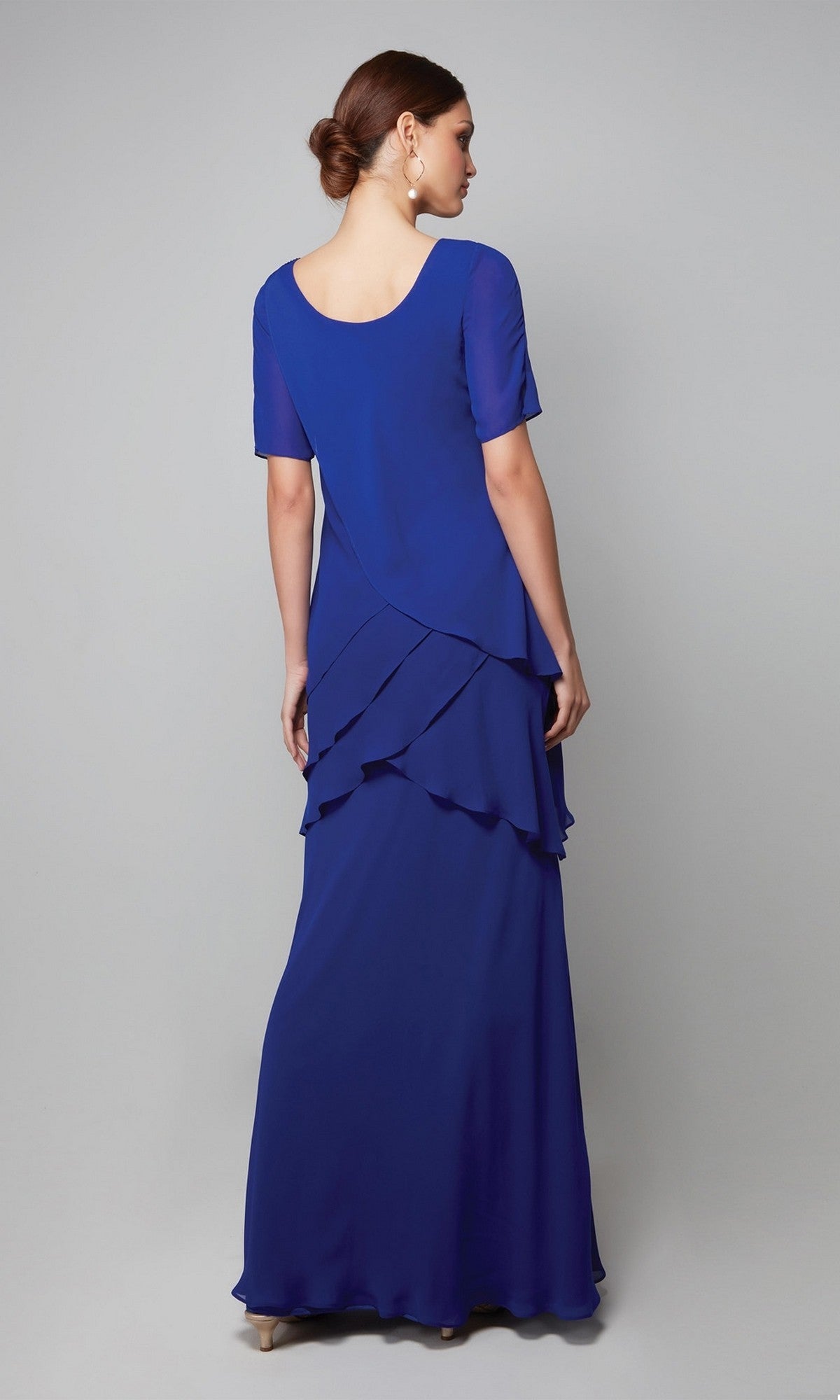 A woman in the Alyce 27593 long formal dress—a royal blue chiffon gown with short sleeves and tiered layers—stands with her back to the camera against a plain background, creating an elegant mother-of-the-bride look.