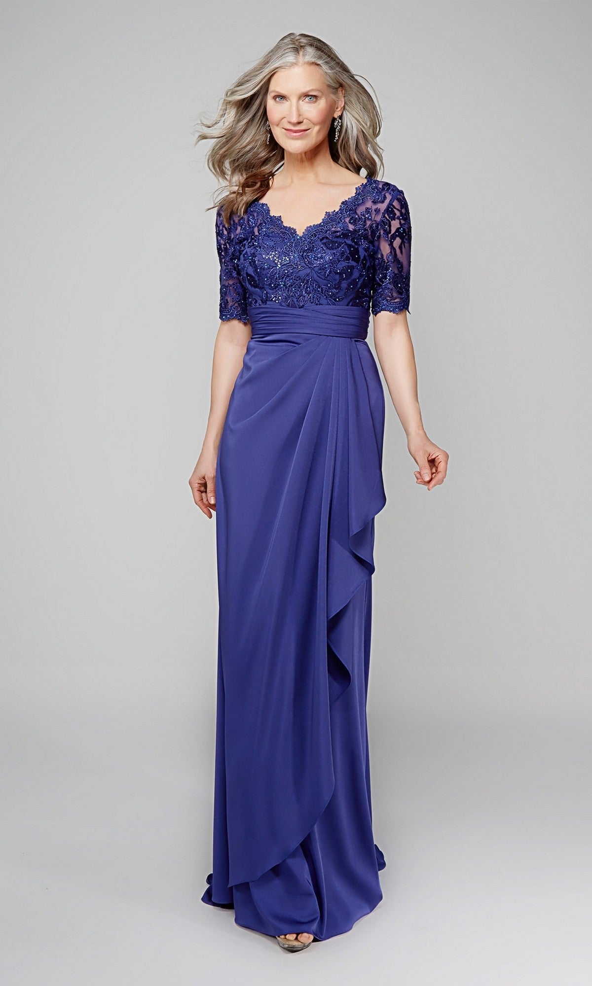 A woman models the Alyce 27595 long formal dress—a royal blue, floor-length mother-of-the-bride gown featuring a lace bodice and short sleeves—against a plain light gray background.