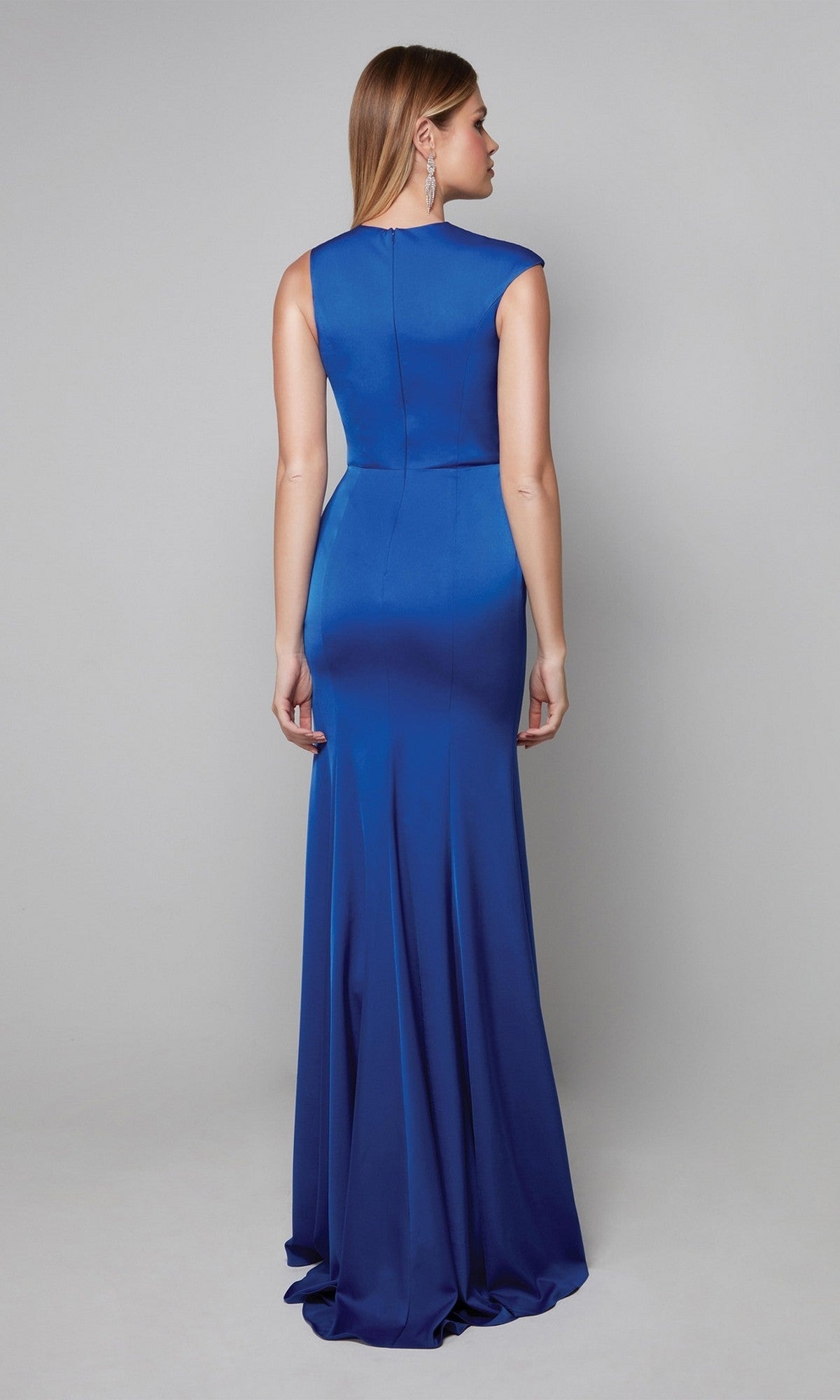 A woman faces away, modeling the Alyce 27598 long formal dress—a royal blue column silhouette with a fitted bodice and gentle flare—against a plain gray background.