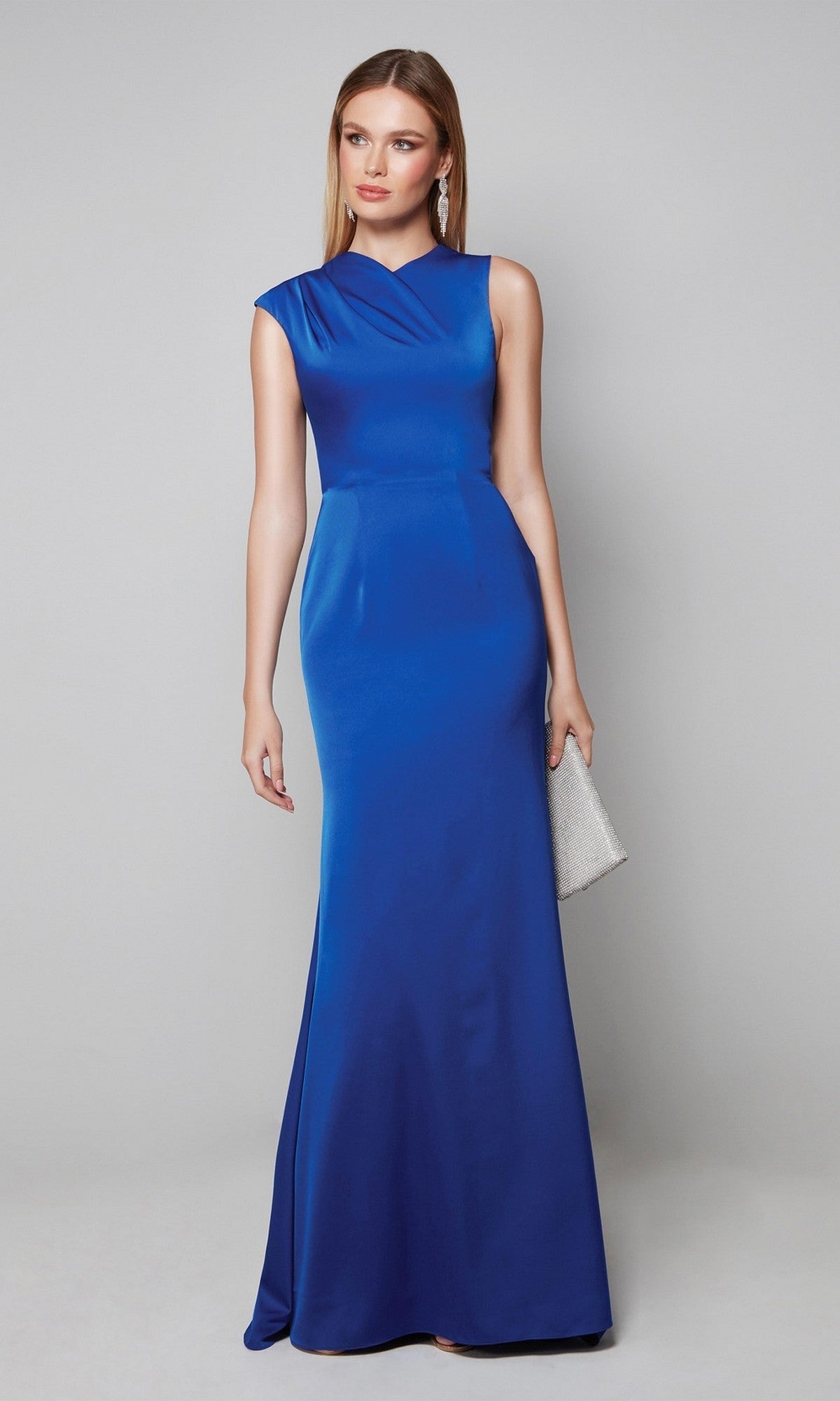 A woman in the Alyce 27598 long formal dress, a sleeveless, floor-length royal blue column gown, holds a silver clutch while standing against a plain light grey background.