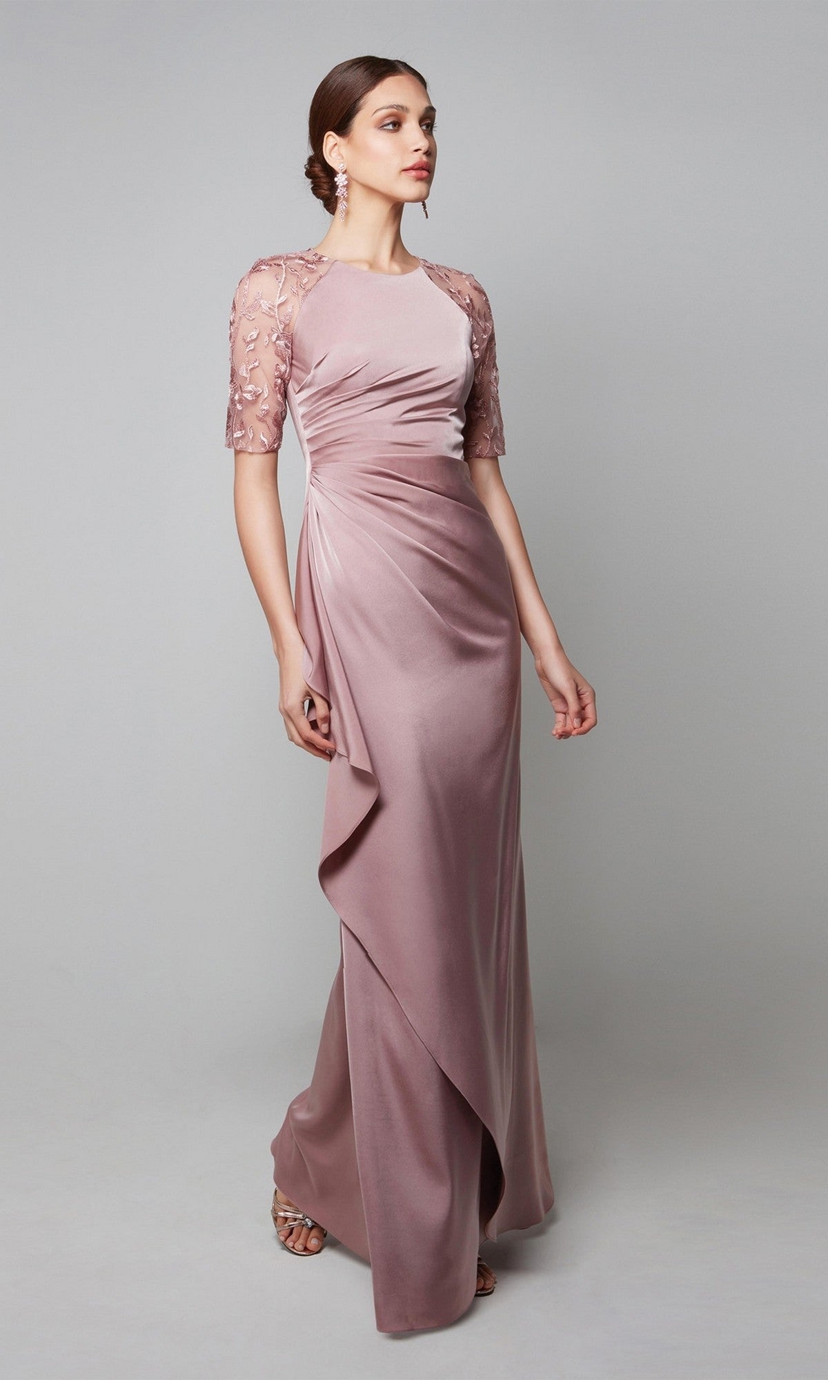A woman stands against a plain gray background wearing the Alyce 27601 long formal dress in heather, featuring sheer embroidered short sleeves and ruched detailing—an ideal choice for a mother-of-the-bride.