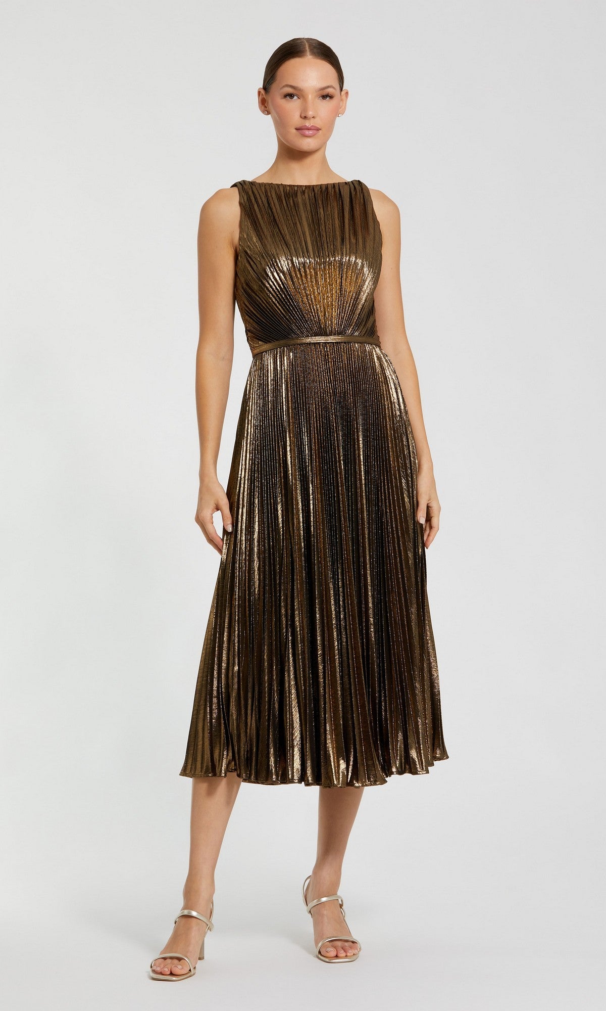 A woman stands against a plain light background wearing the Mac Duggal 27611 Midi Party Dress in Antique Gold, which features metallic pleats, paired with silver high-heeled sandals.