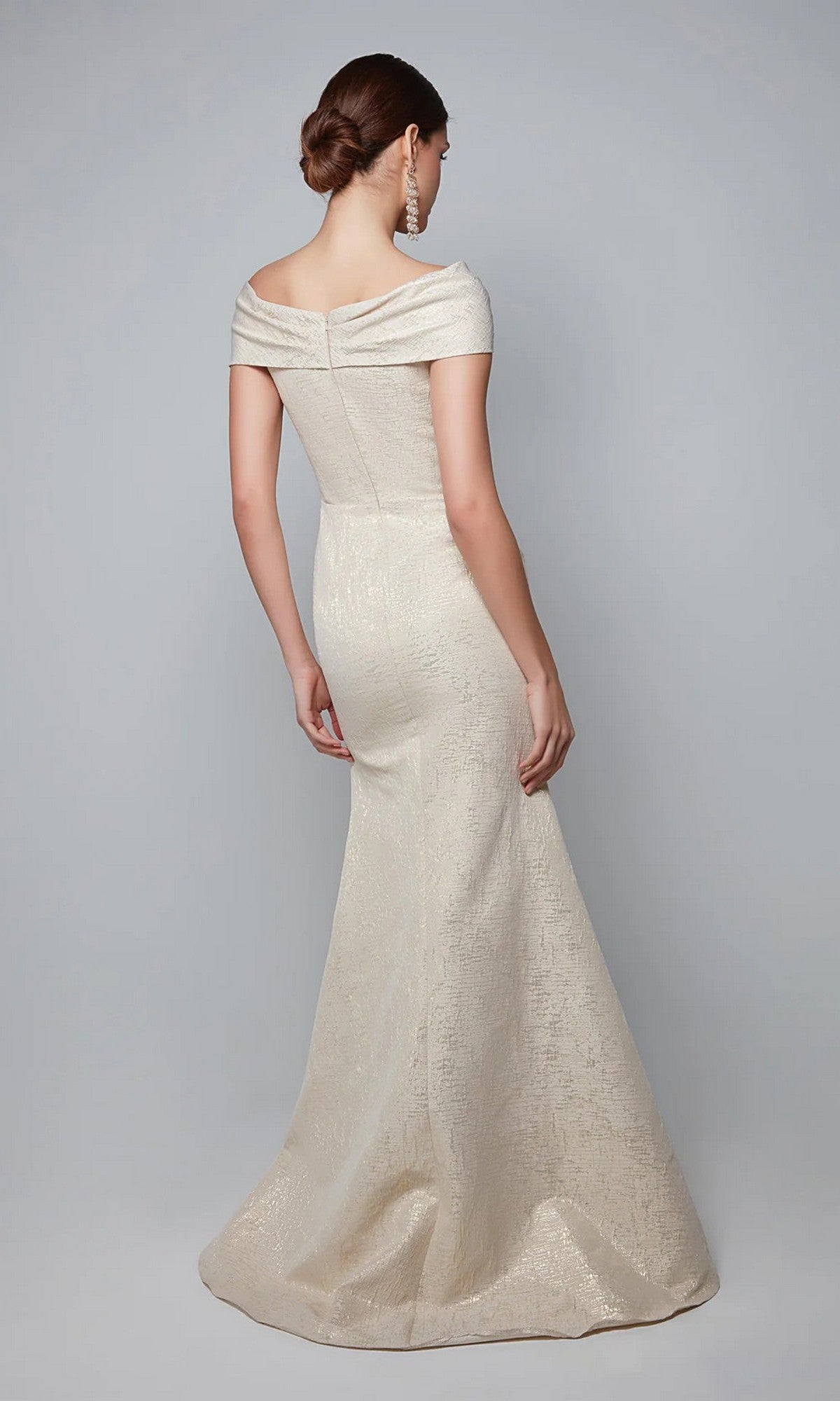 Woman wearing the Alyce 27613 long formal dress, an off-the-shoulder, floor-length cream jacquard gown with a subtle textured pattern, stands with her back to the camera.