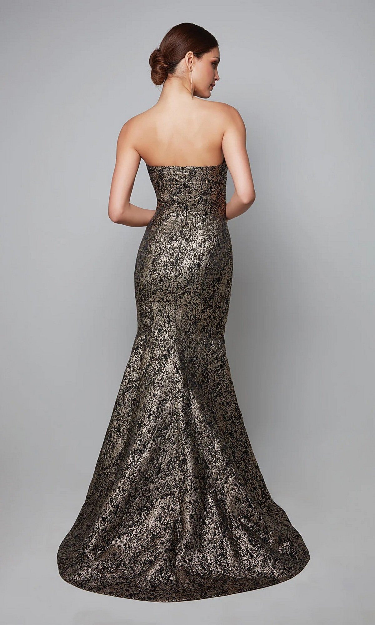 A woman faces away, wearing the Alyce 27621 long formal dress—a strapless jacquard gown with a metallic mermaid silhouette and textured pattern. Her hair is in a low bun, complementing the evening look against a plain gray background.