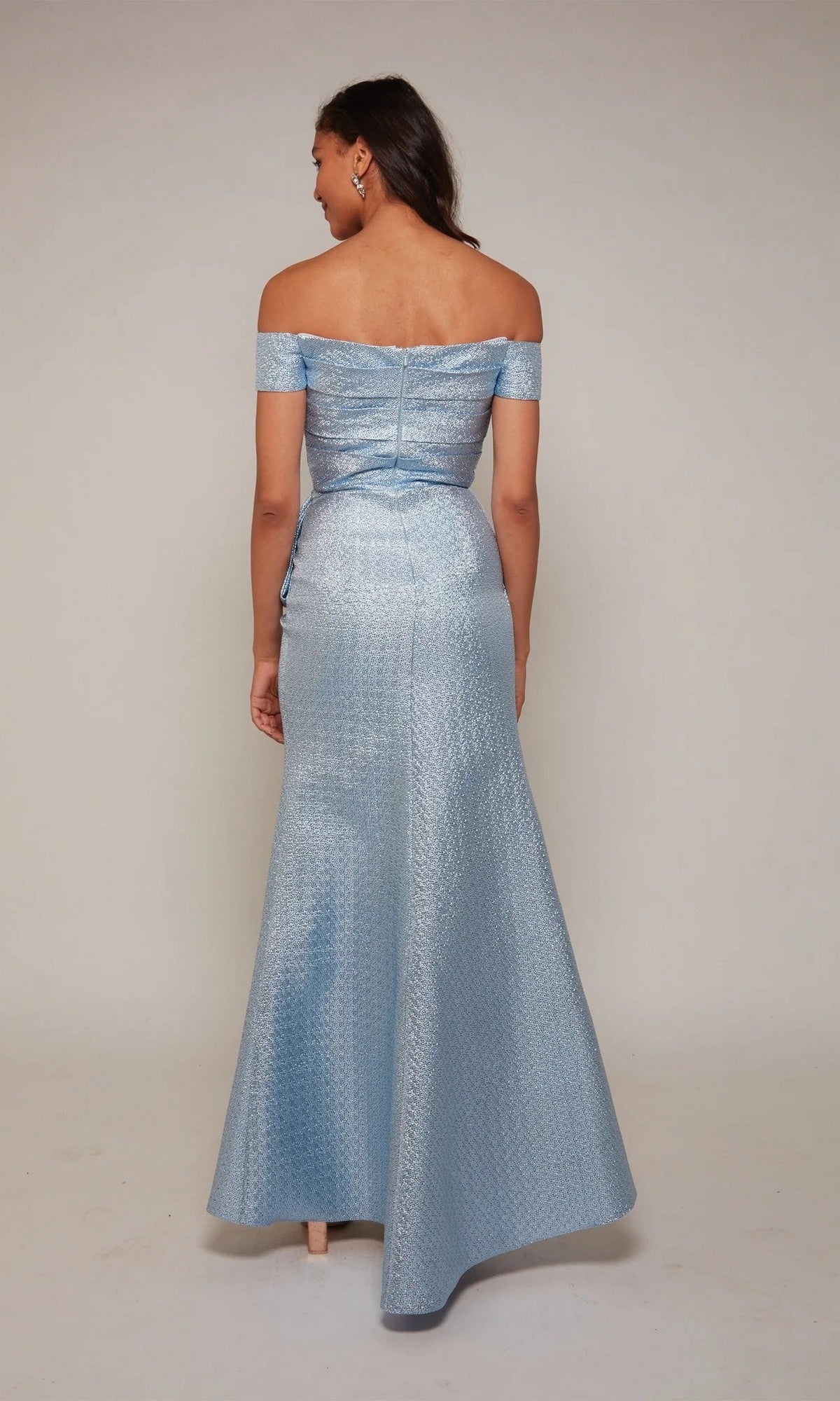 A woman stands with her back to the camera wearing the Alyce 27639 Long Formal Dress, a light blue, off-the-shoulder jacquard evening gown with a subtle textured pattern and floor-length elegance.