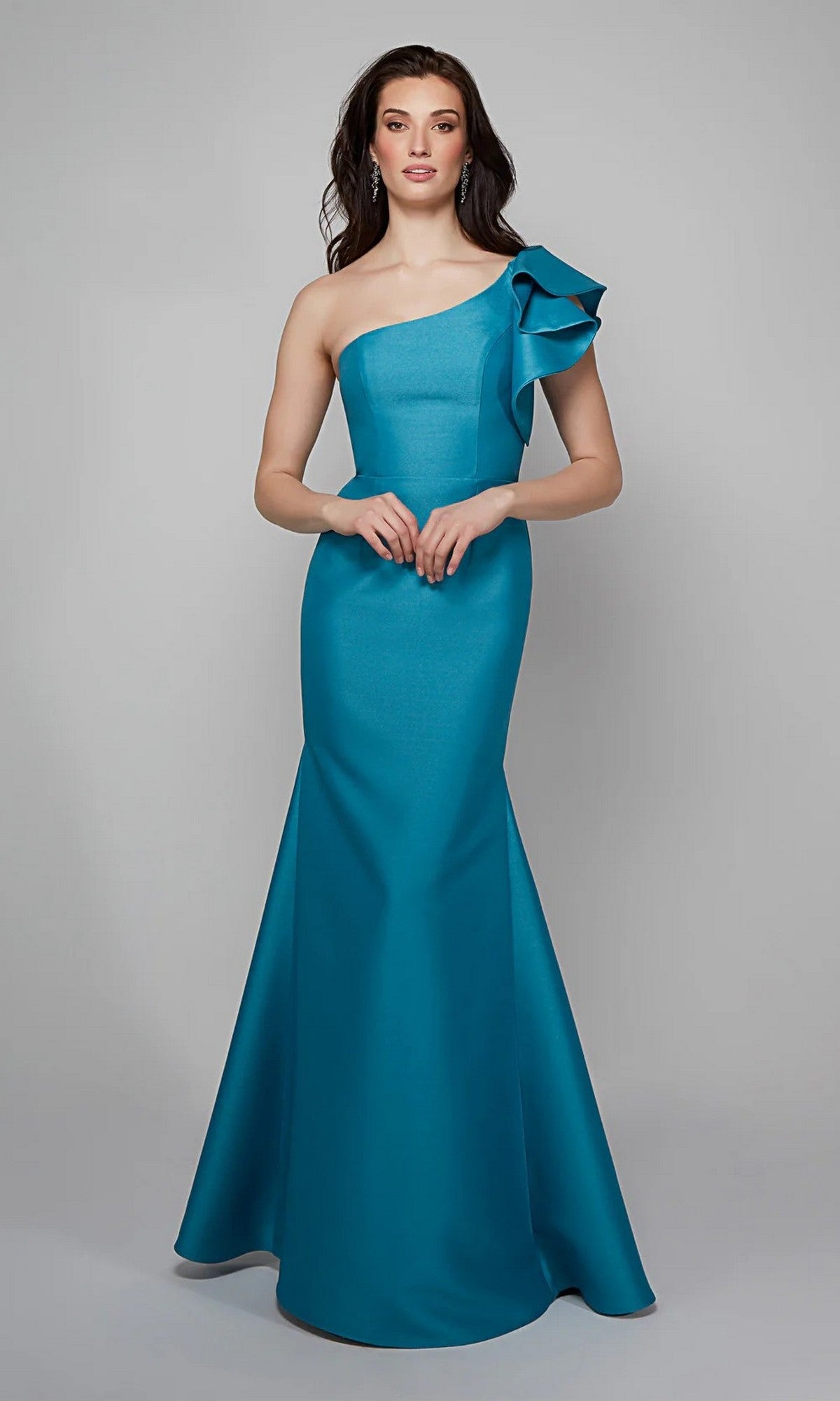A woman stands against a plain gray background wearing the Alyce 27641 long formal dress in sea green, featuring a floor-length, one-shoulder design with a large ruffle detail on the shoulder.