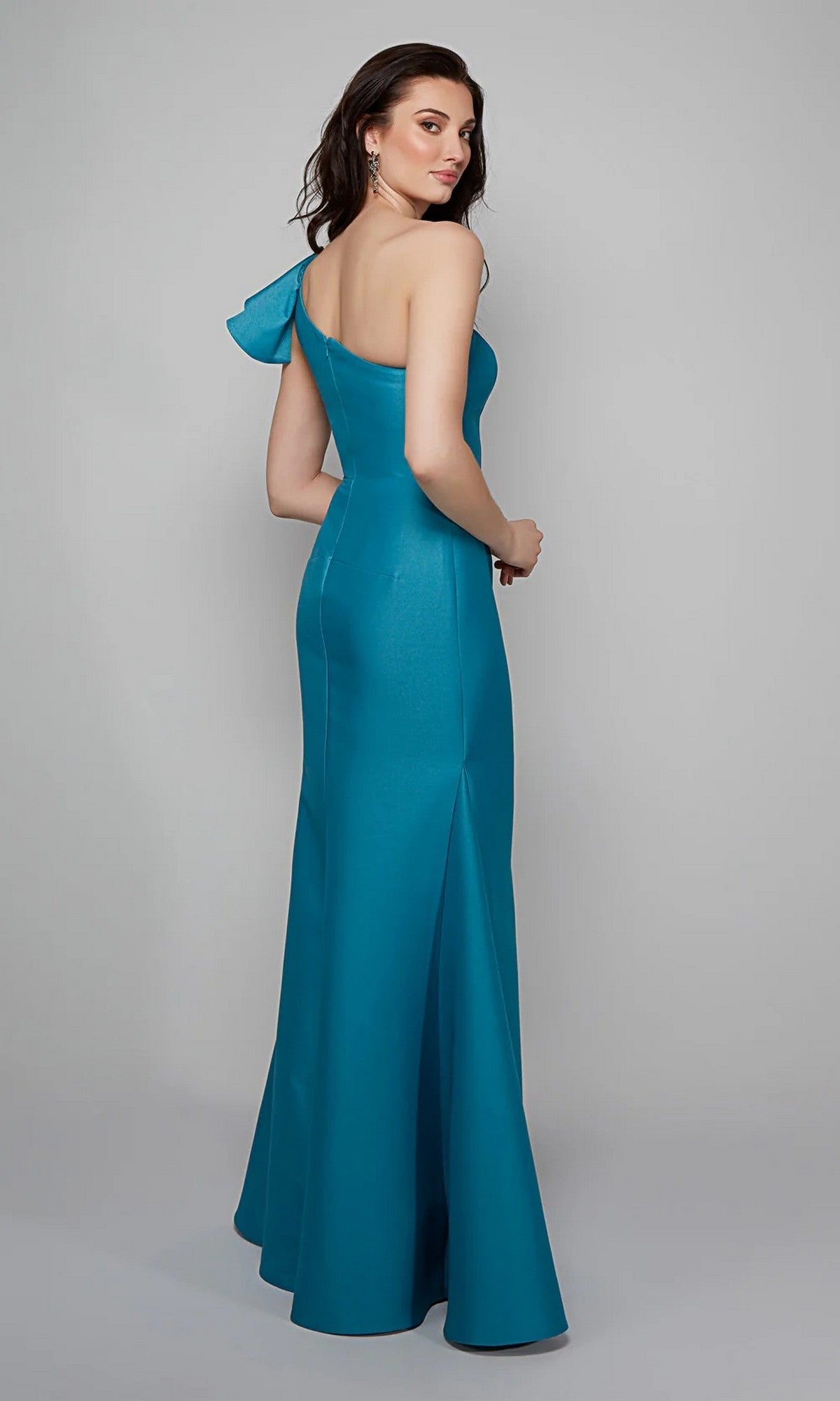 A woman models the Alyce 27641 long formal dress—a teal, one-shoulder gown in lustrous Mikado—facing backward and looking over her shoulder against a plain gray backdrop.