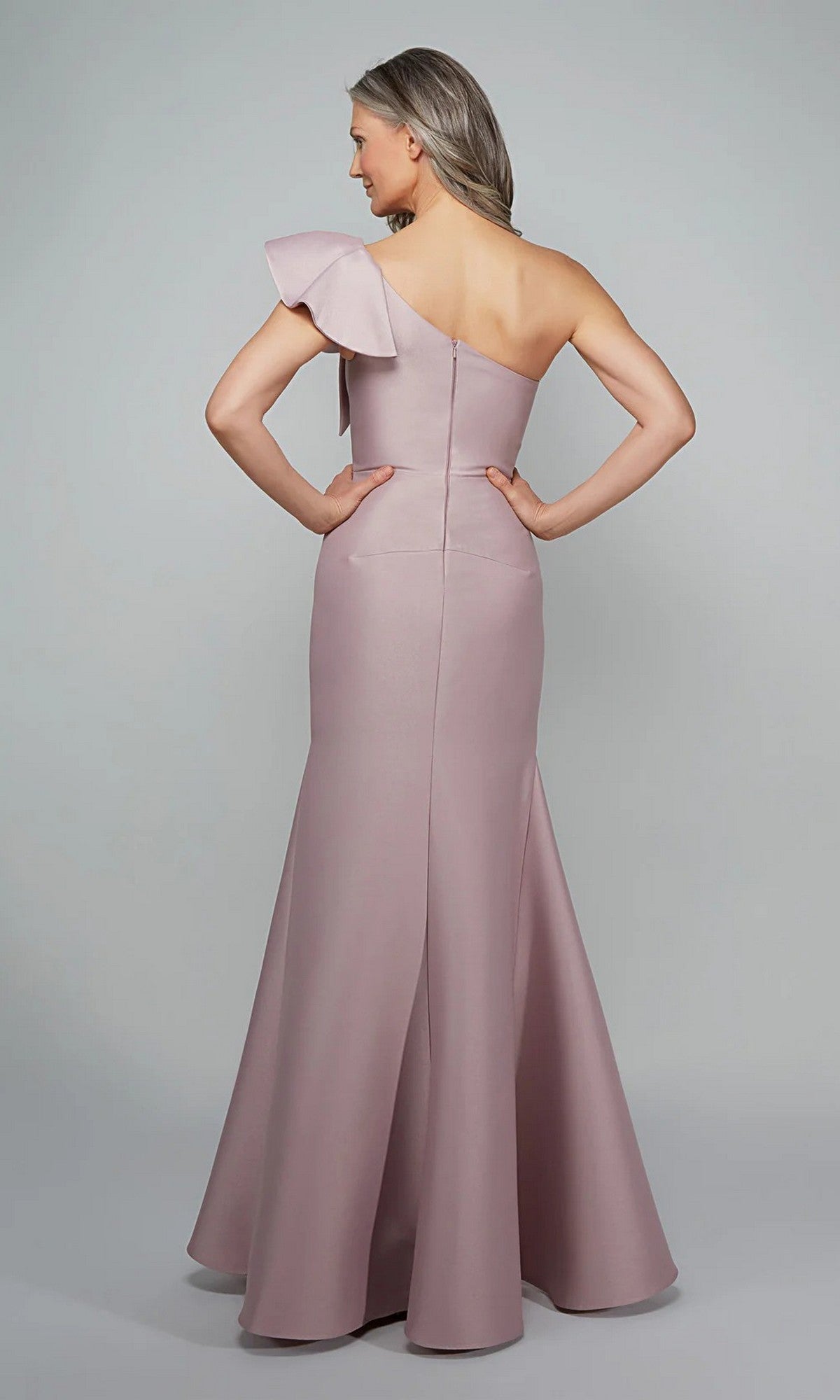 A woman showcases the fitted back and flared hem of the mauve, one-shoulder Alyce 27641 long formal dress with a ruffled sleeve—an elegant choice for a mother-of-the-bride look.