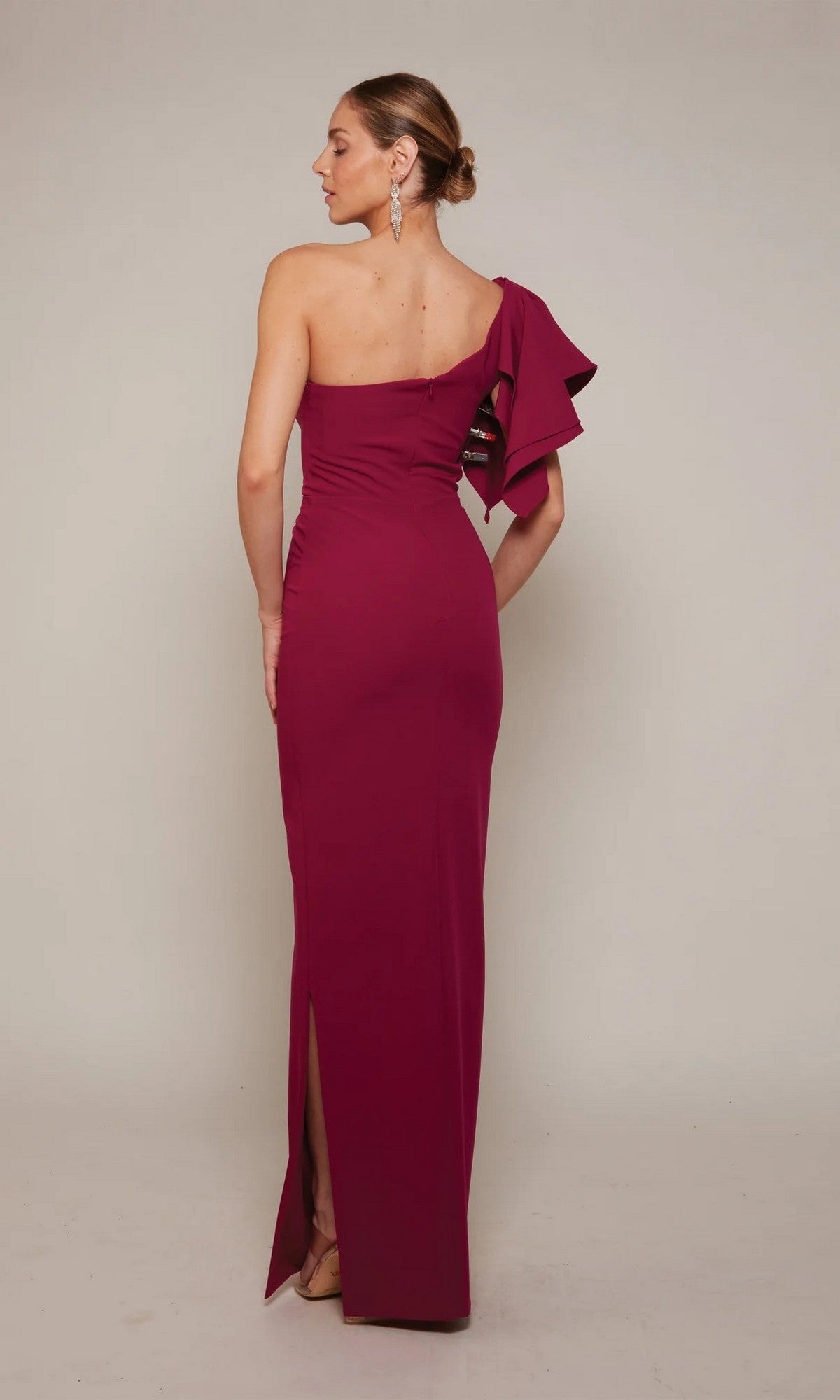 A woman models the Alyce 27644 long formal dress in magenta stretch satin, featuring a fitted silhouette and one-shoulder ruffle, standing with her back to the camera against a plain background.