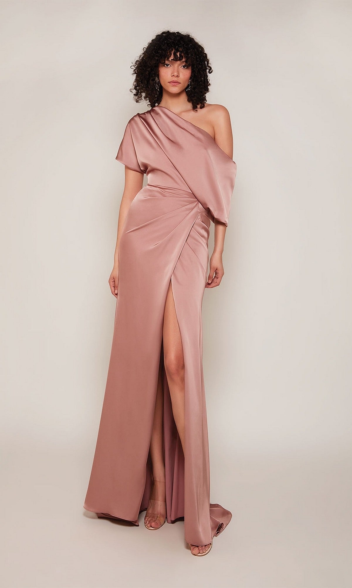 A woman wears the Alyce 27652 long formal dress in Vintage Rose, a one-shoulder satin gown with a thigh-high slit, standing against a plain light background.