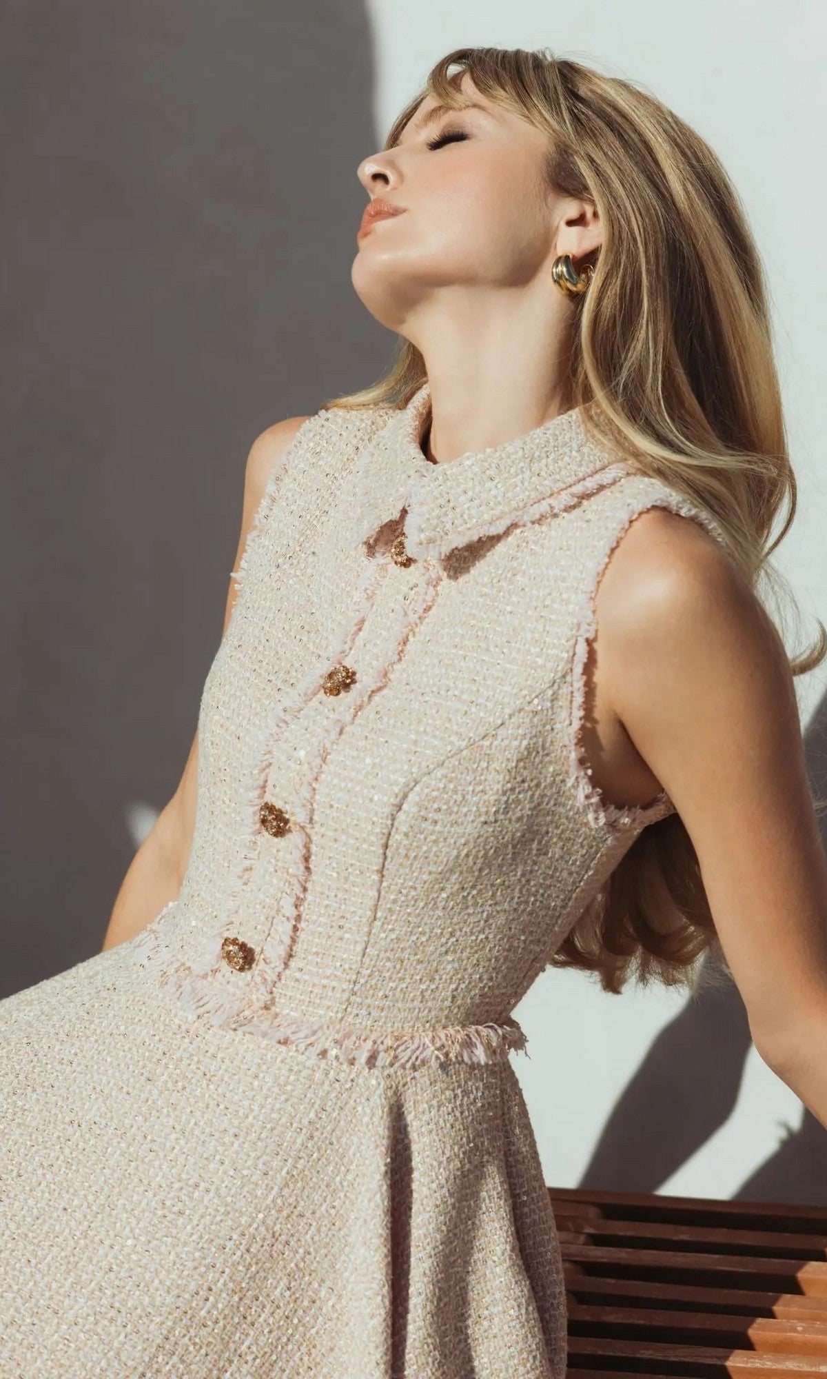 A woman wears the Mac Duggal 27658 Semi-Formal Midi Dress, sitting on a wooden bench with her head tilted back and eyes closed against a white background.