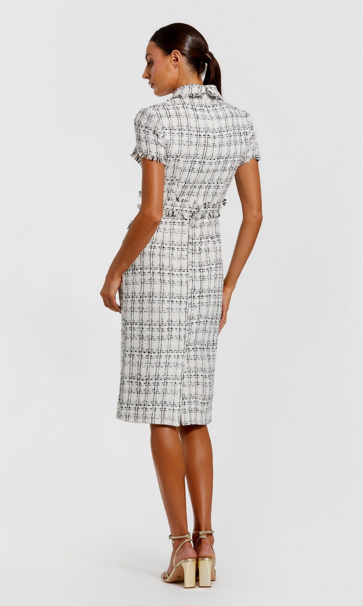 A woman stands with her back to the camera, wearing the Mac Duggal 27660 knee-length day dress featuring a black plaid pattern, short sleeves, jeweled buttons down the back, and light-colored heeled sandals.