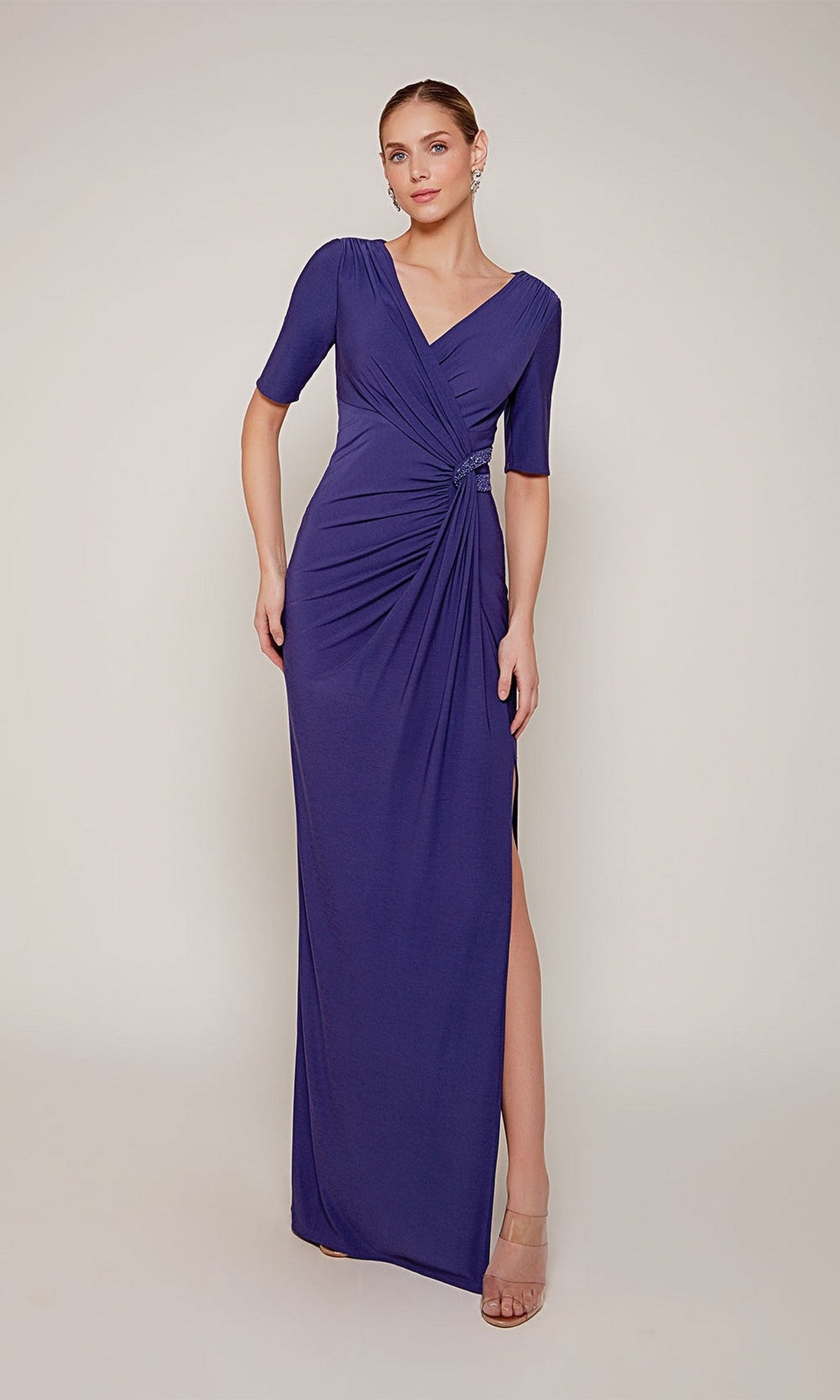A woman stands against a plain background wearing the Alyce 27682 long formal dress, featuring short sleeves, a v-neckline, floor-length design, and side slit.