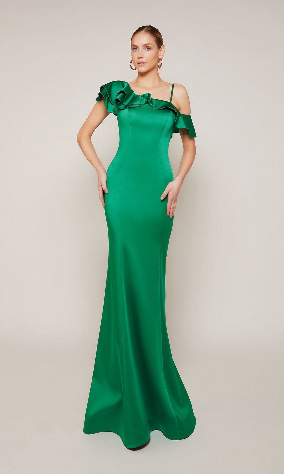 A woman models the Alyce 27691 long formal dress—an emerald green satin gown with a fitted silhouette, thin shoulder straps, and an asymmetrical ruffled neckline—set against a plain background.