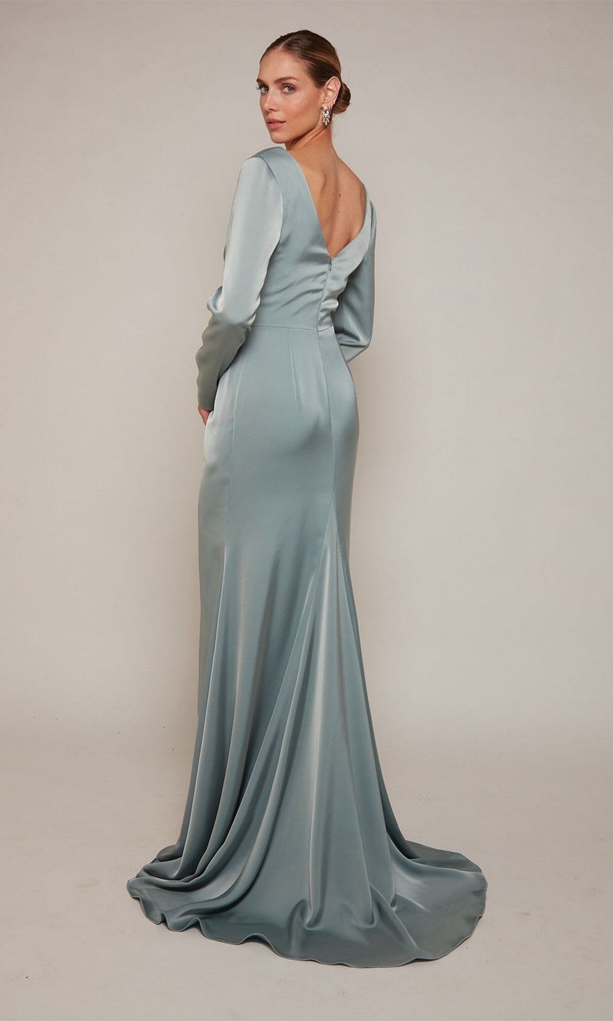 Wearing the Alyce 27694, a long formal dress in light blue satin with long sleeves and an open back, a woman stands against a plain background—an elegant mother-of-the-bride look.