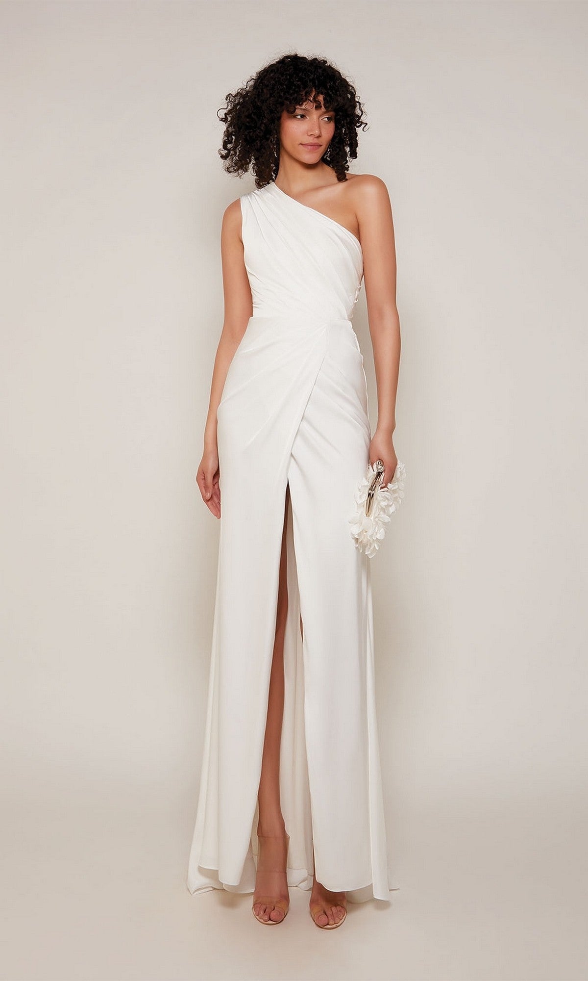 A woman stands against a plain background wearing the Alyce 27697 long formal dress in diamond white, featuring a one-shoulder satin design with a thigh-high slit and holding a small white clutch—ideal for prom or any formal event.