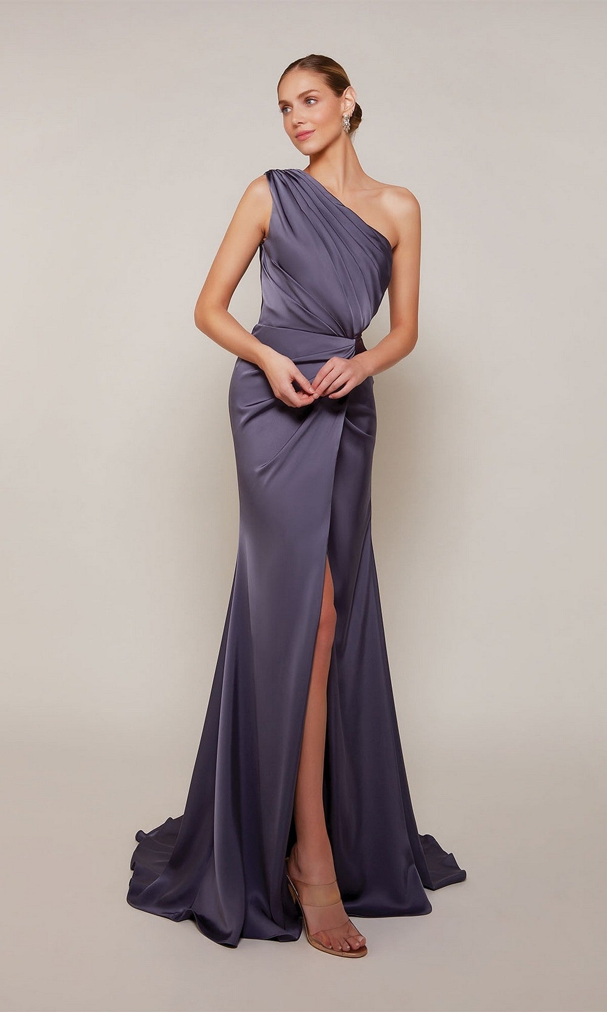 A woman wears the Alyce 27697 long formal dress in Storm Cloud, a floor-length, one-shoulder satin gown with a thigh-high slit—ideal for prom or any formal event, shown against a plain light background.