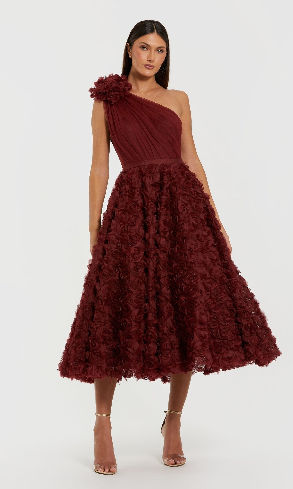 A woman wearing the Mac Duggal 27698 Midi Wine Wedding Guest Dress, featuring one shoulder, a textured floral midi skirt, a large flower detail on the shoulder, and paired with nude high-heeled sandals.