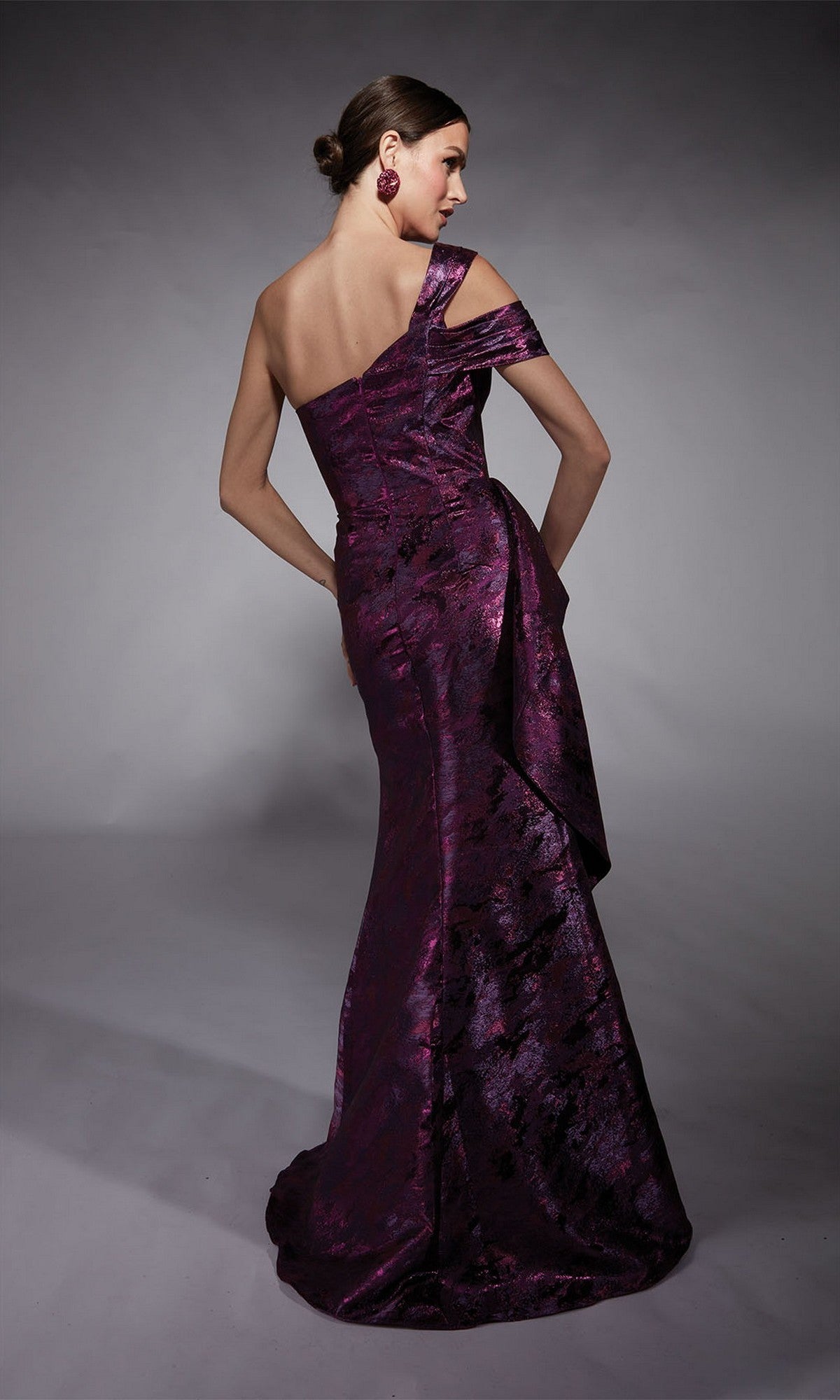 A woman stands with her back turned against a gray background, wearing the Alyce 27701—a floor-length, off-the-shoulder purple formal dress with a textured pattern—an elegant modern choice for mothers of the bride.