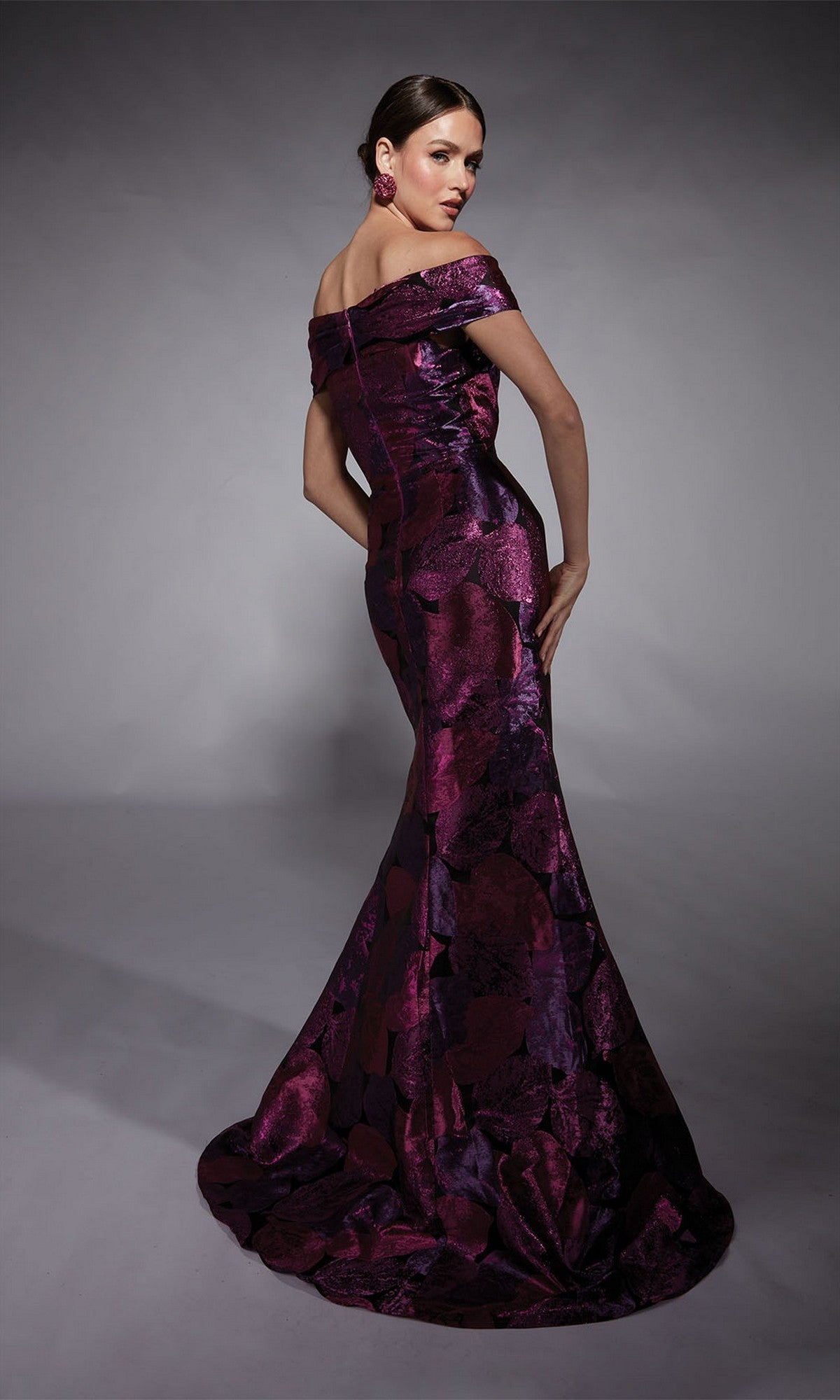 A woman poses in the Alyce 27702 long formal dress, an off-the-shoulder, floor-length jacquard gown with a purple and black floral pattern and fitted silhouette—ideal for the modern mother of the bride—against a gray background.