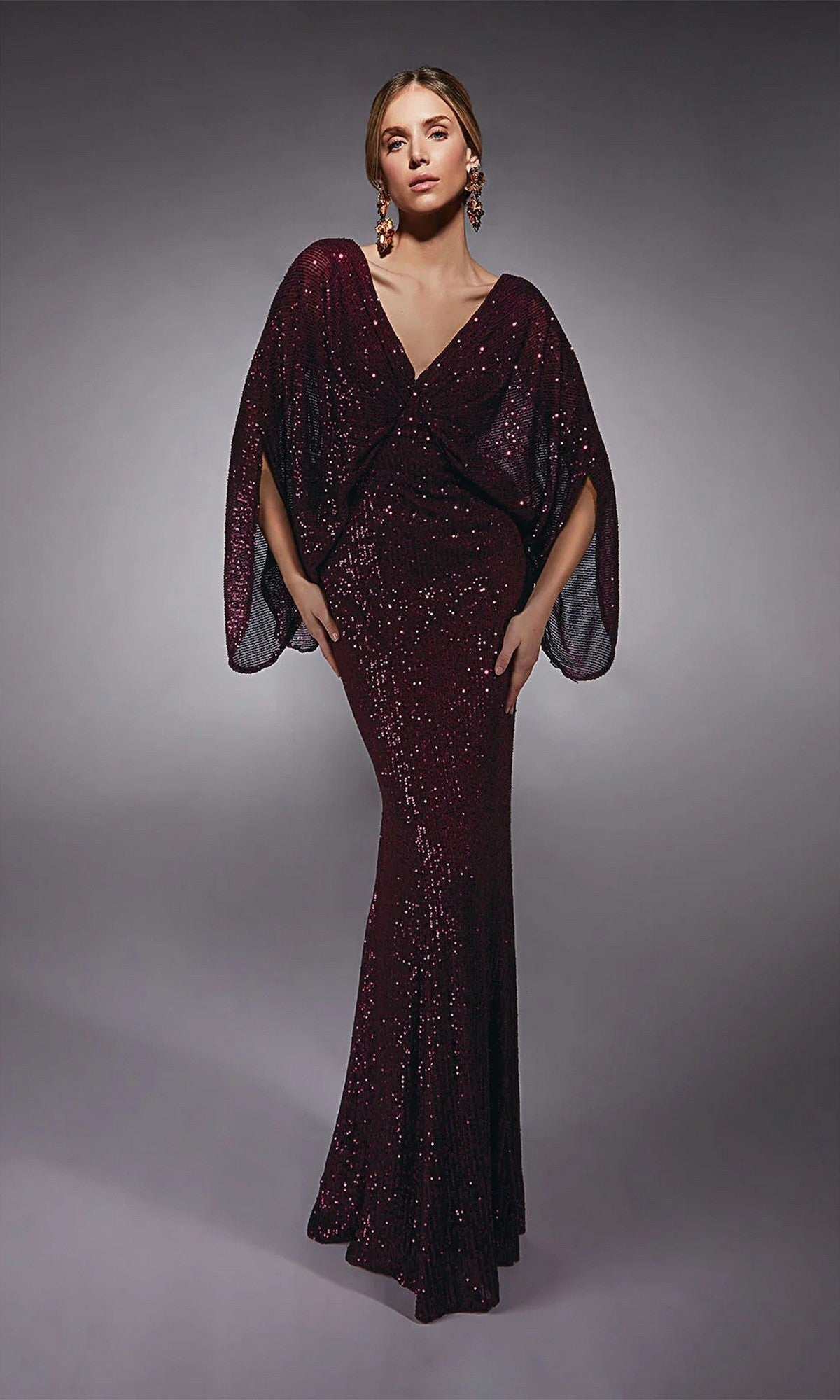 A woman poses against a plain gray background wearing the Alyce 27703 long formal dress in dark burgundy, featuring floor-length style and batwing sleeves.